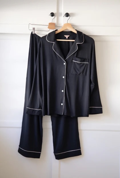 Black with white lining Eberjey pajama button up top and pannts hanging against white wall. 