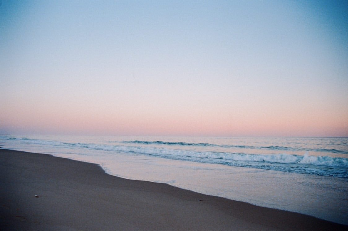 Purple and pink beach sunset over crashing waves.