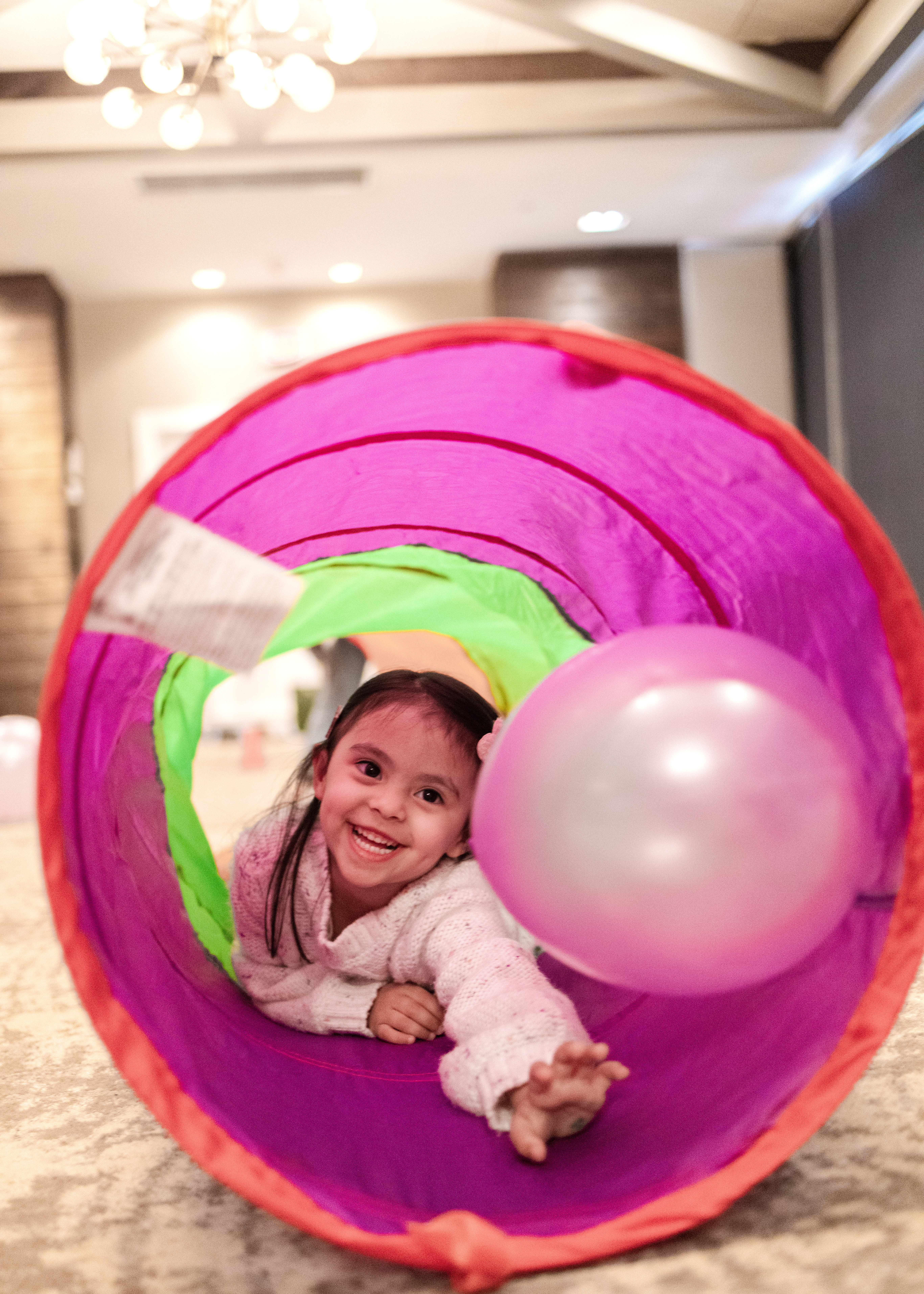 Little girl excitedly chasing a ball through a tunnel with a huge smile.