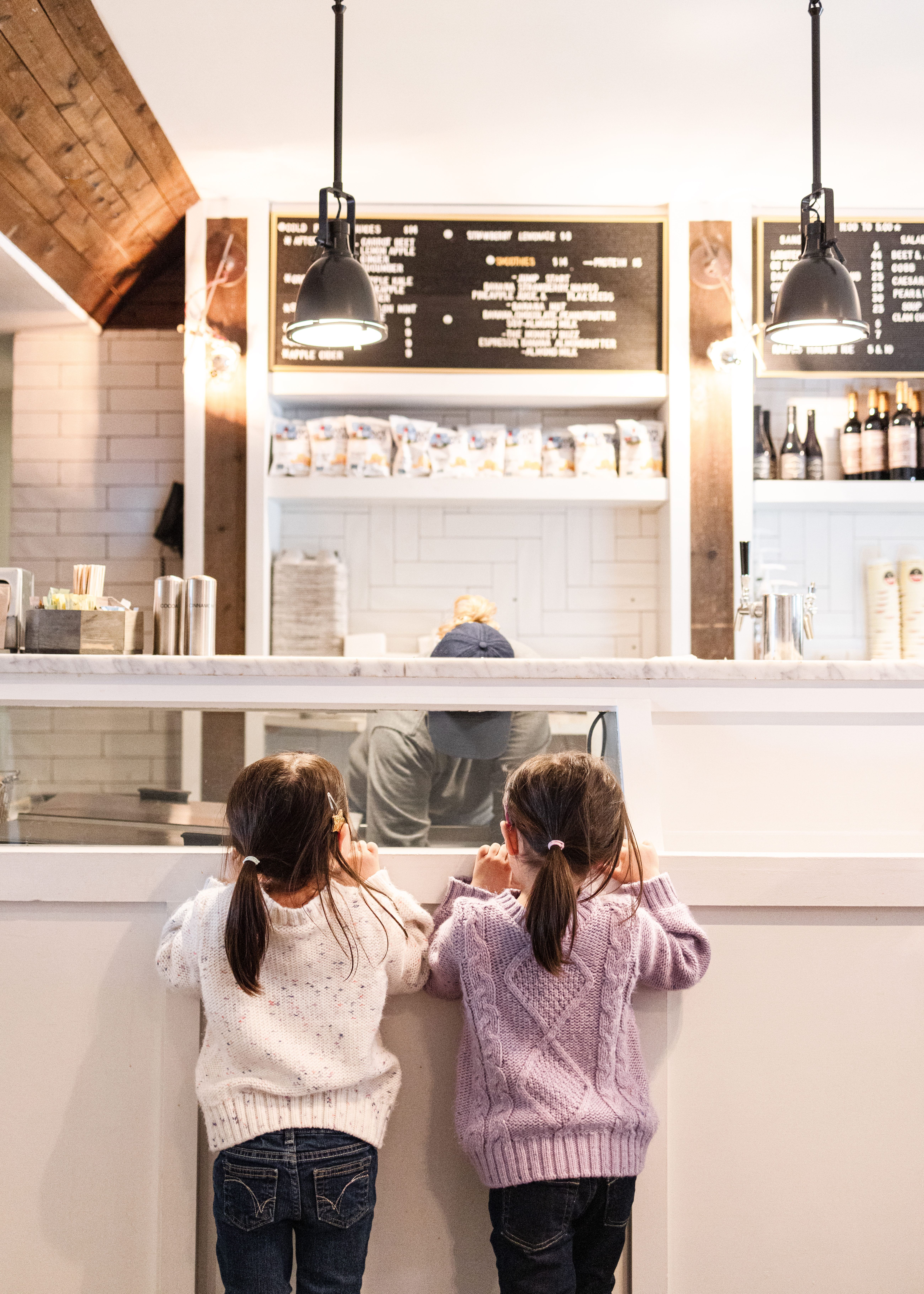 Two girls eagerly awaiting ice cream at the counter while server scoops.