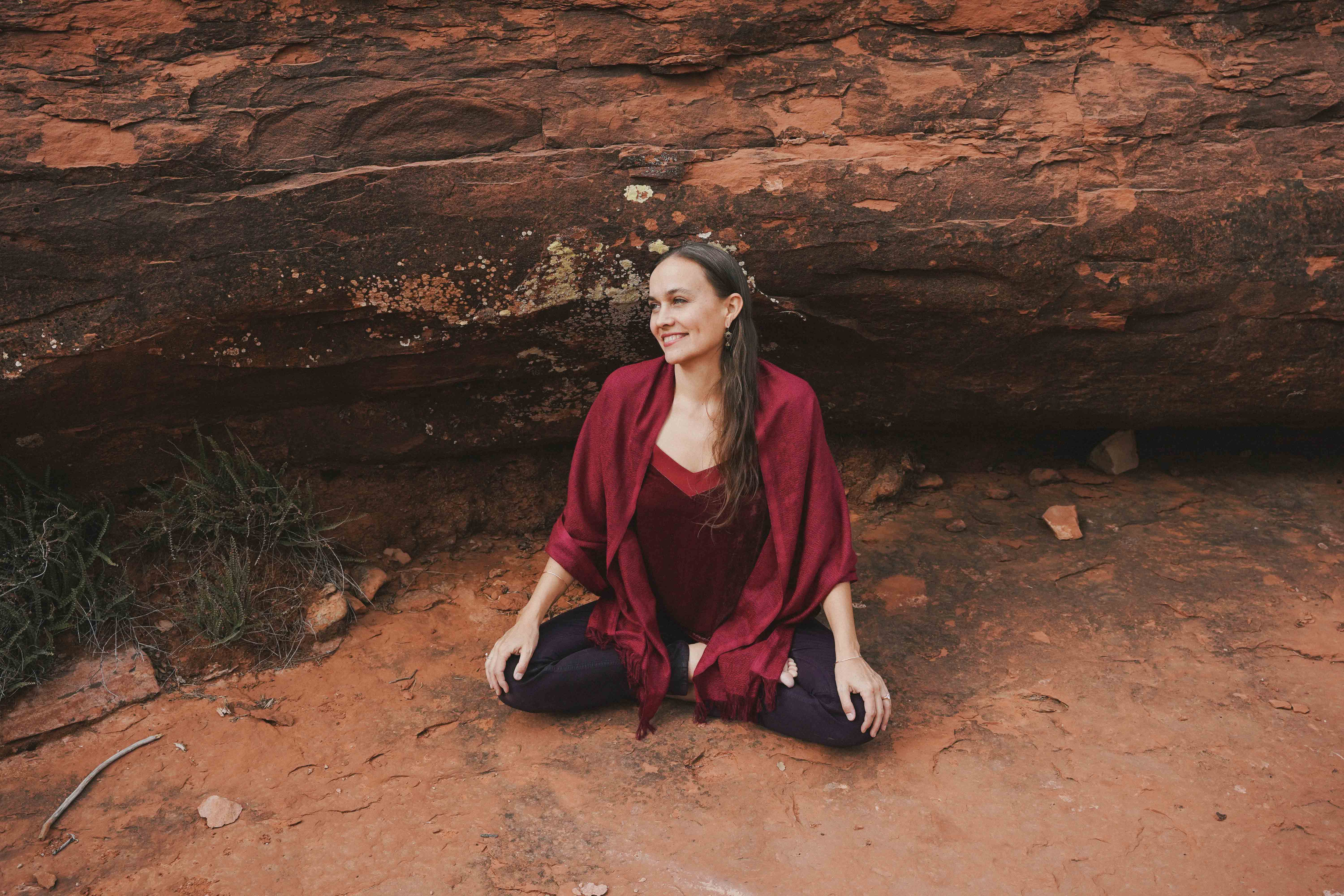 Katie Hess, founder of LOTUSWEI, sitting and smiling amidst red desert rocks.