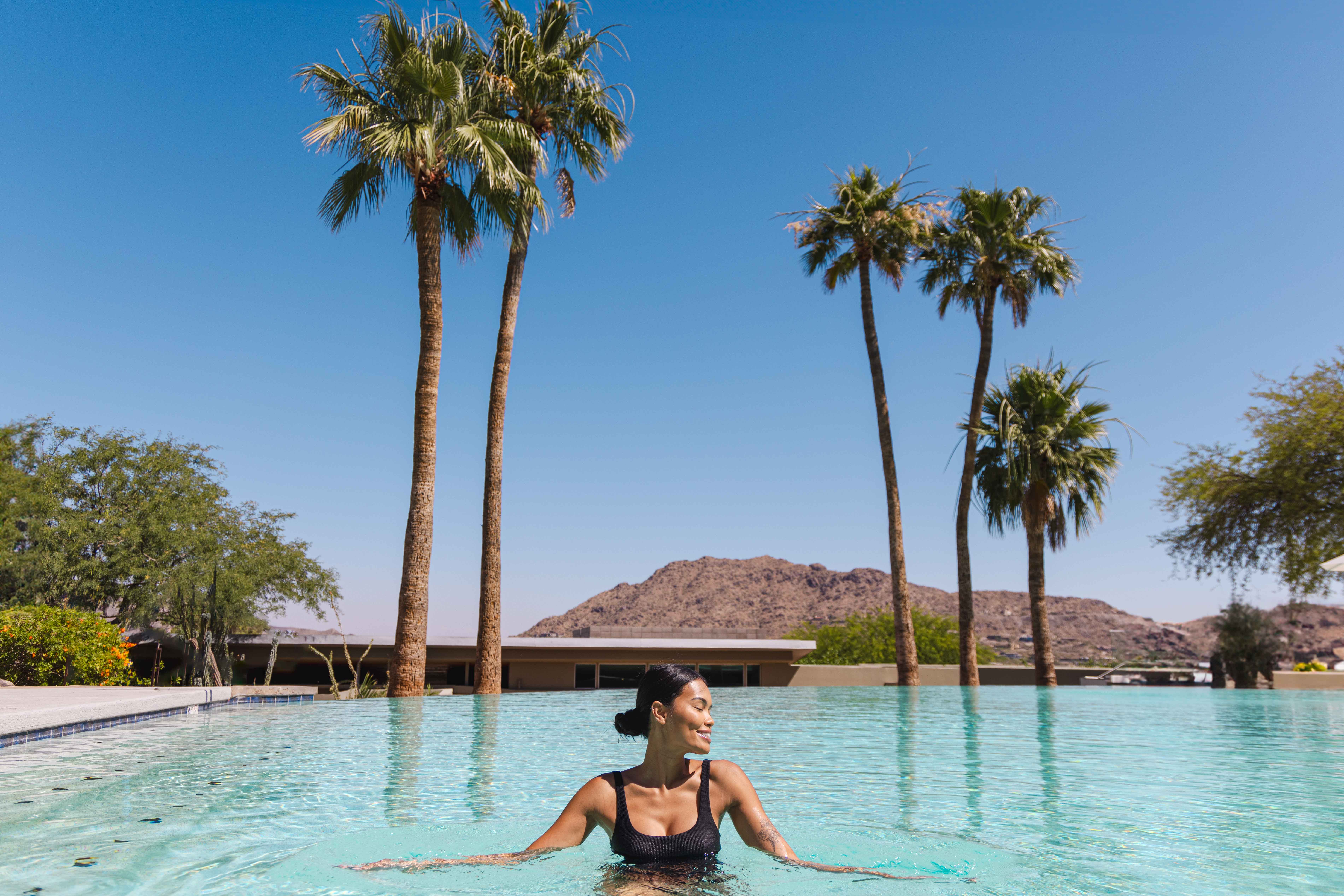 Woman smiling and enjoying a dip in the Infinity Pool with beautiful desert views of surrounding mountains.