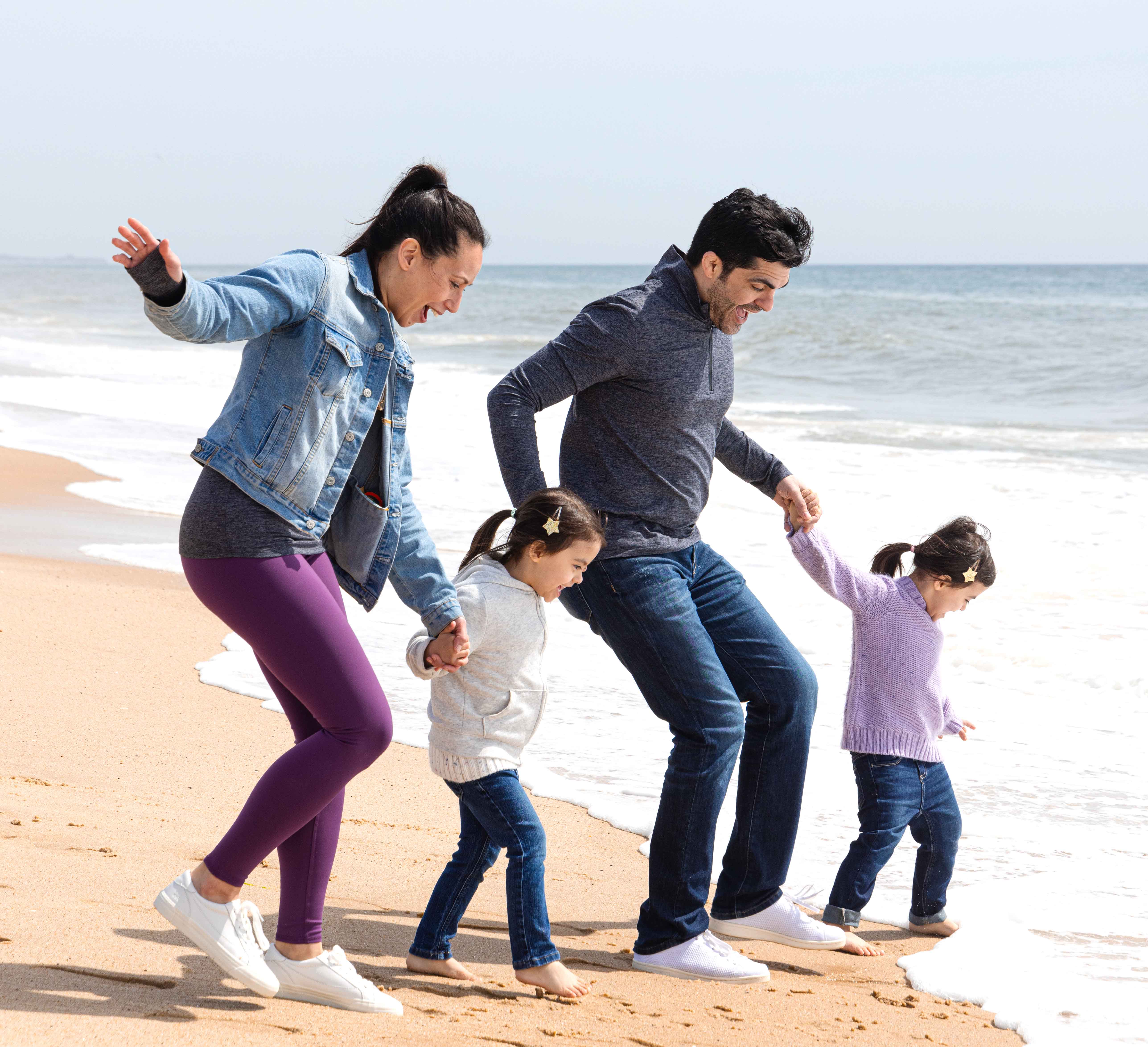 Husband, wife and two daughters tiptoeing towards the breaking waves on the beach.