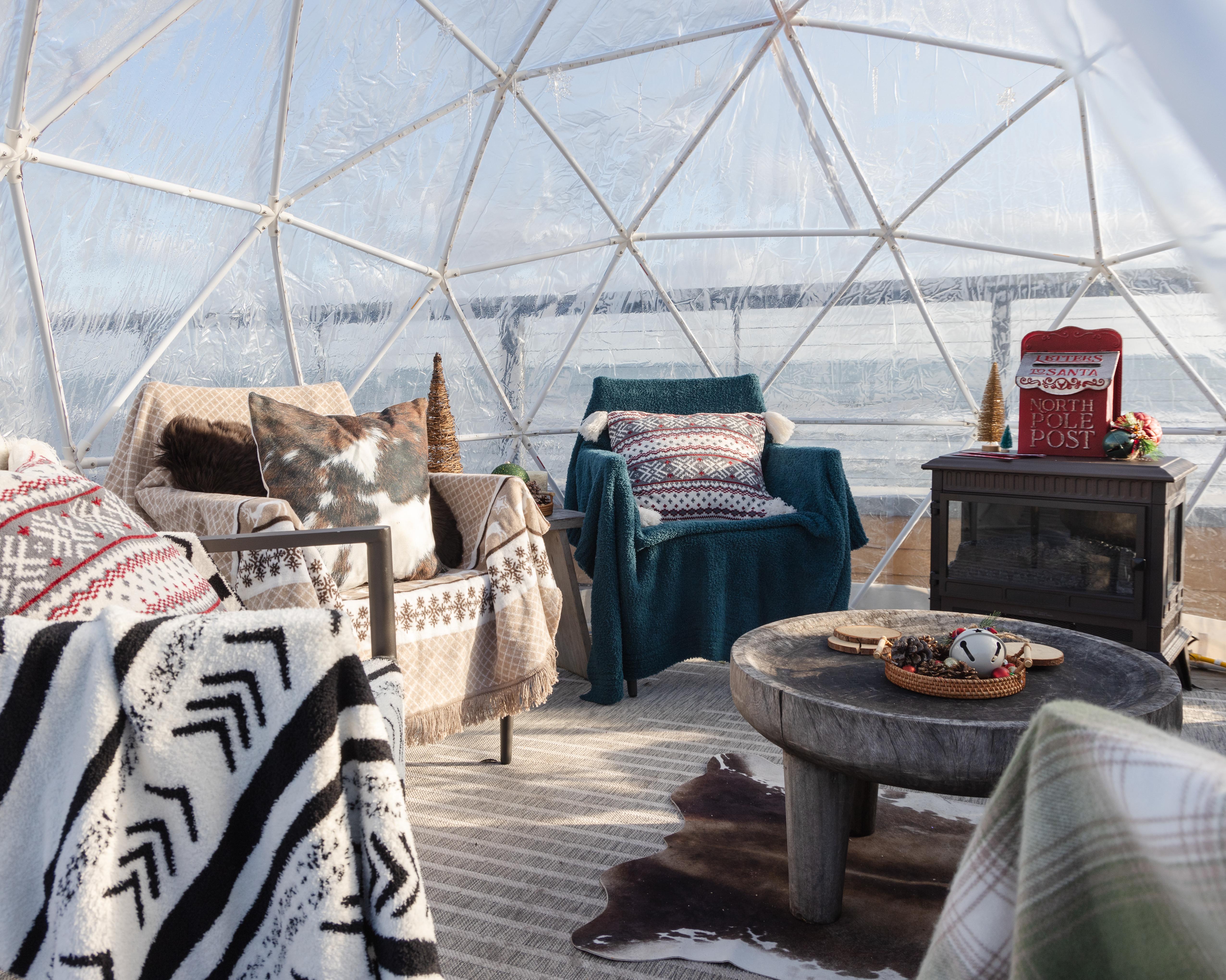 Interior of igloo with chairs, pillows, Barefoot Dreams blankets, table, fire place and holiday decor..