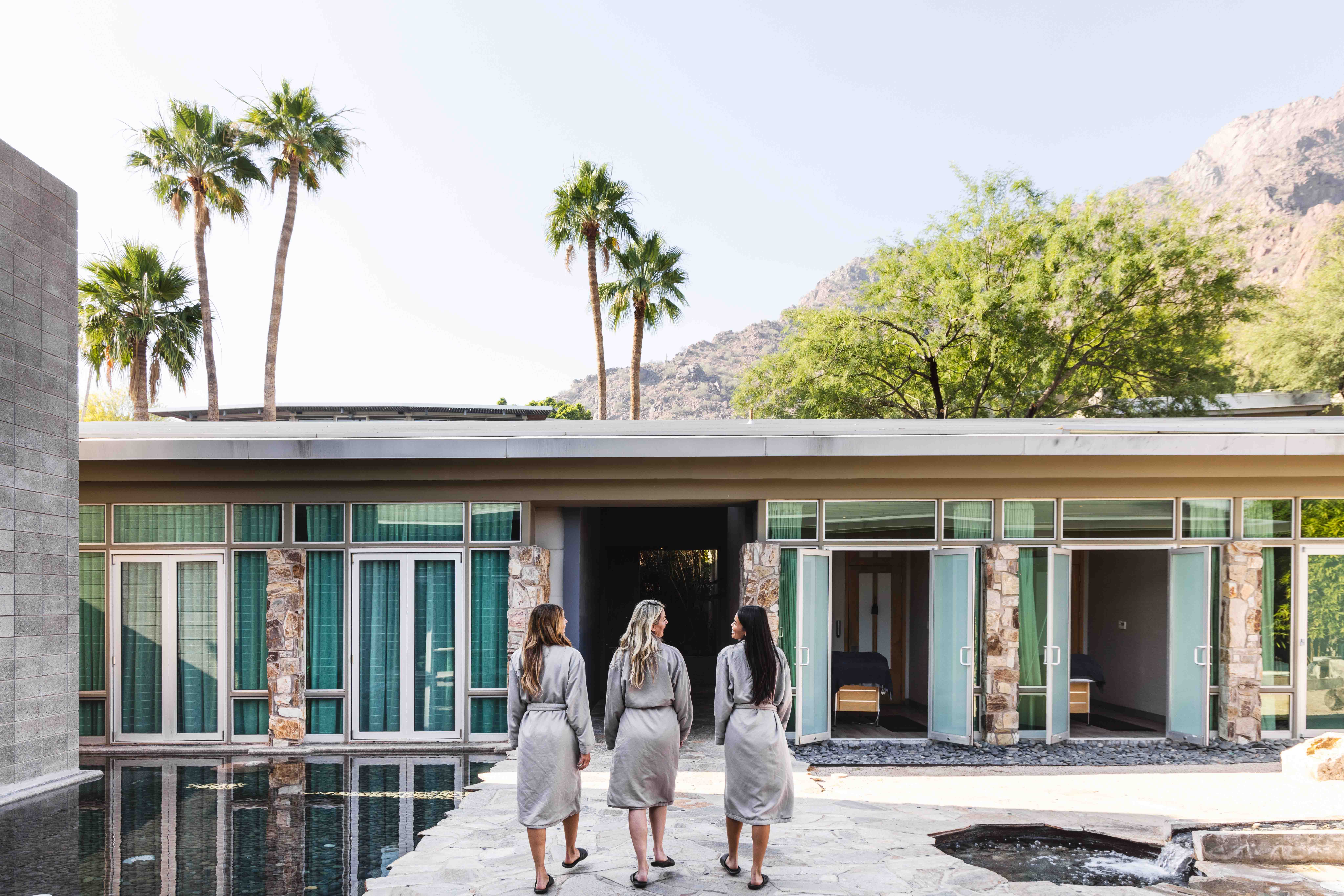 Three women in robes walking through Sanctuary Spa's Zen Garden with indoor/outdoor treatment rooms.