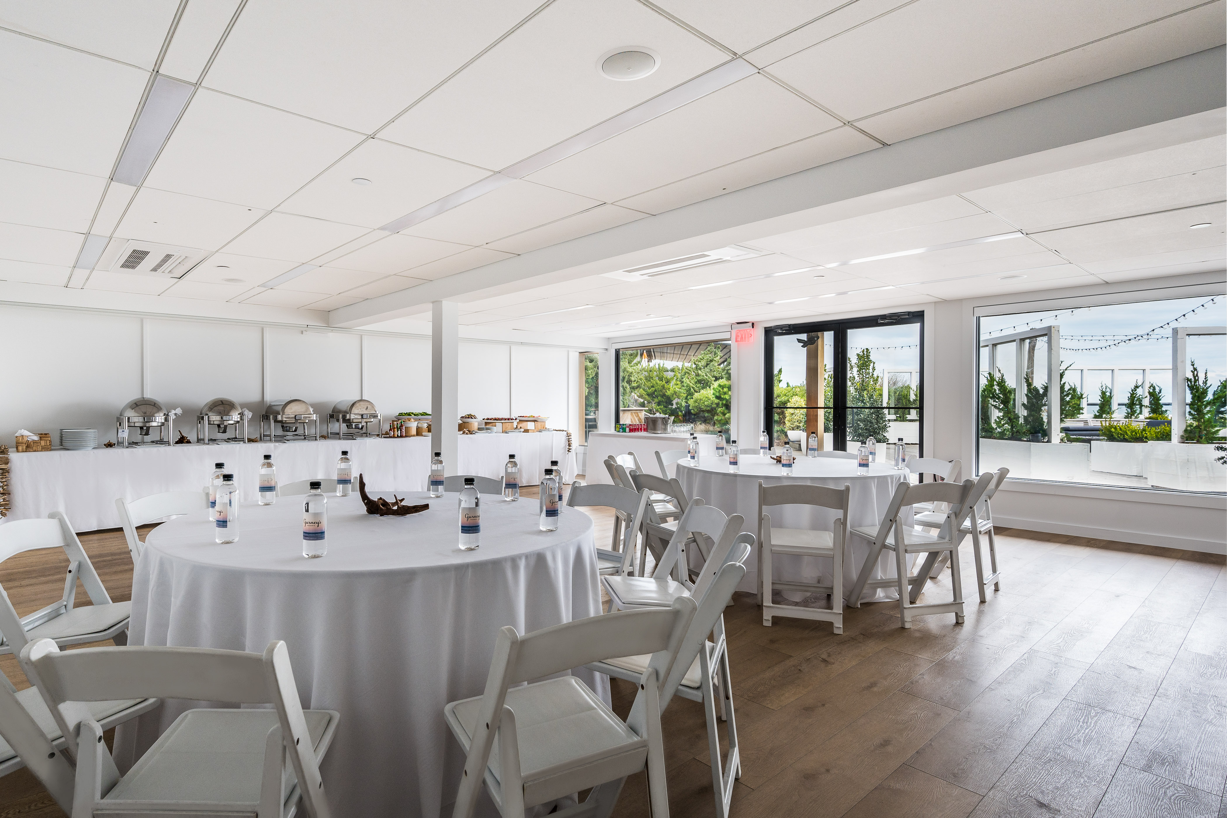 Latitude meeting venue with round top tables, white linens, white chairs and buffet table setup in back.