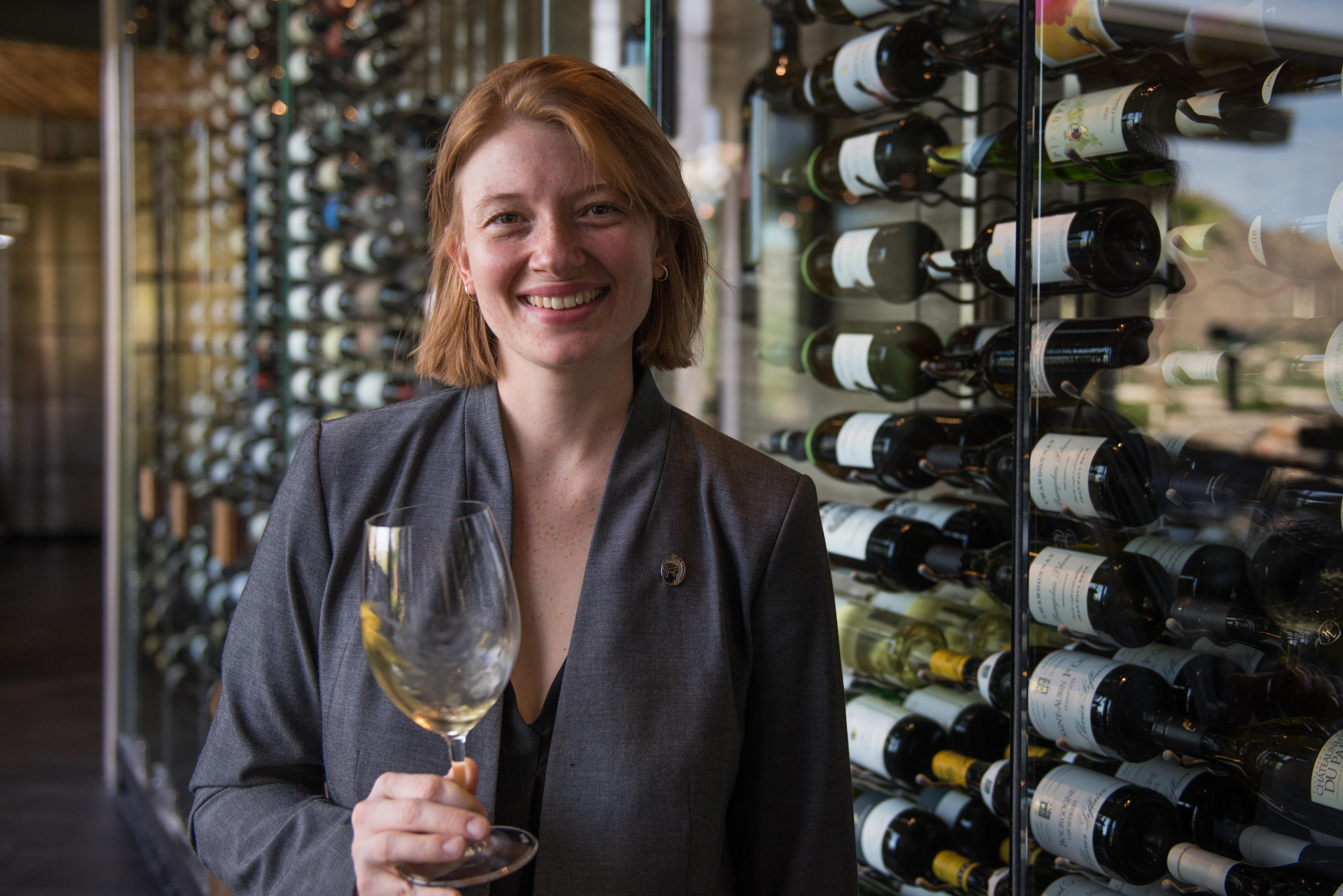 Sanctuary Sommelier Laura Bruno in a grey blazer swirling a glass of white wine.