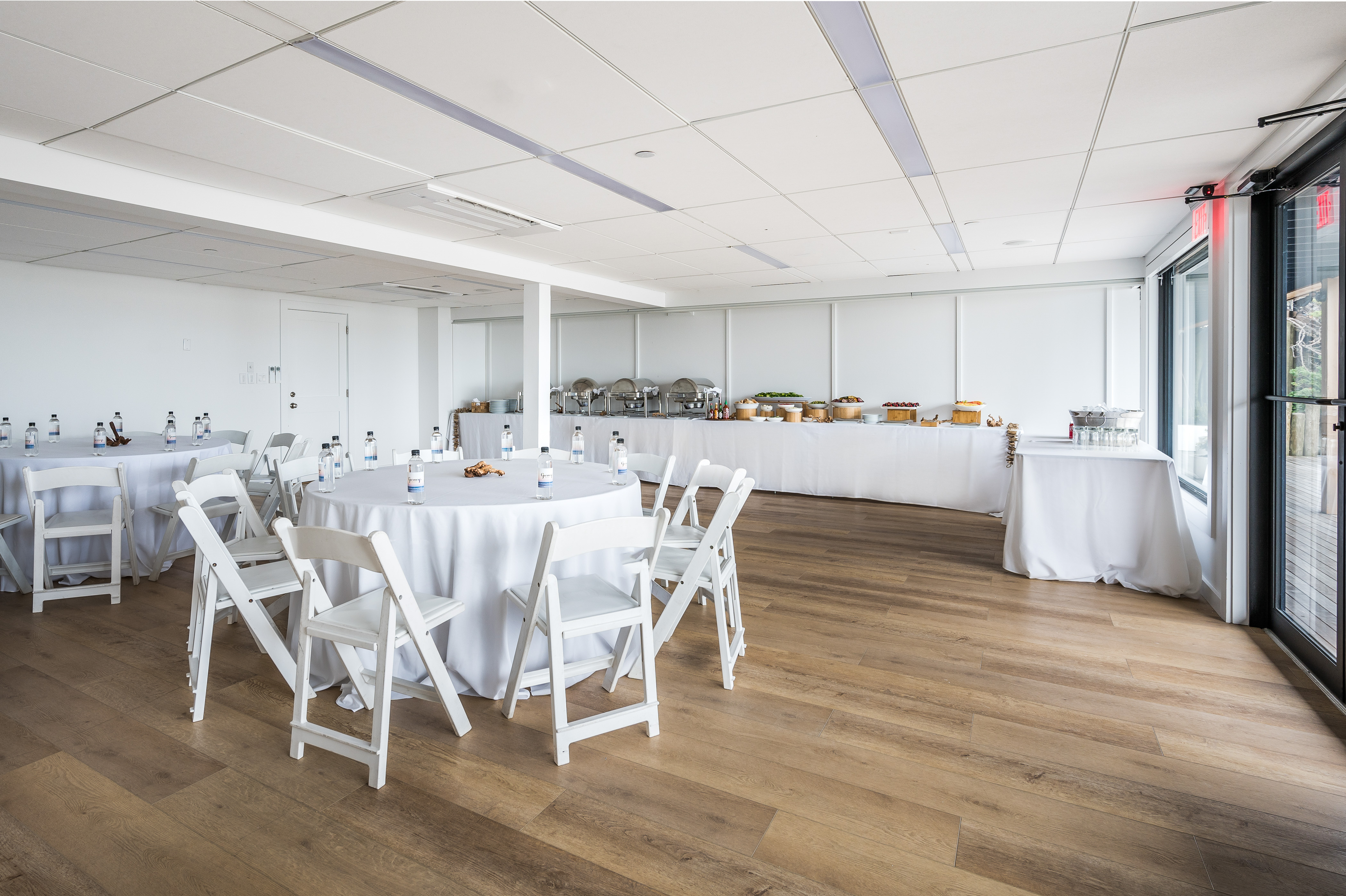 Longitude meeting venue with round top tables, white linens, white chairs and buffet table setup in back.