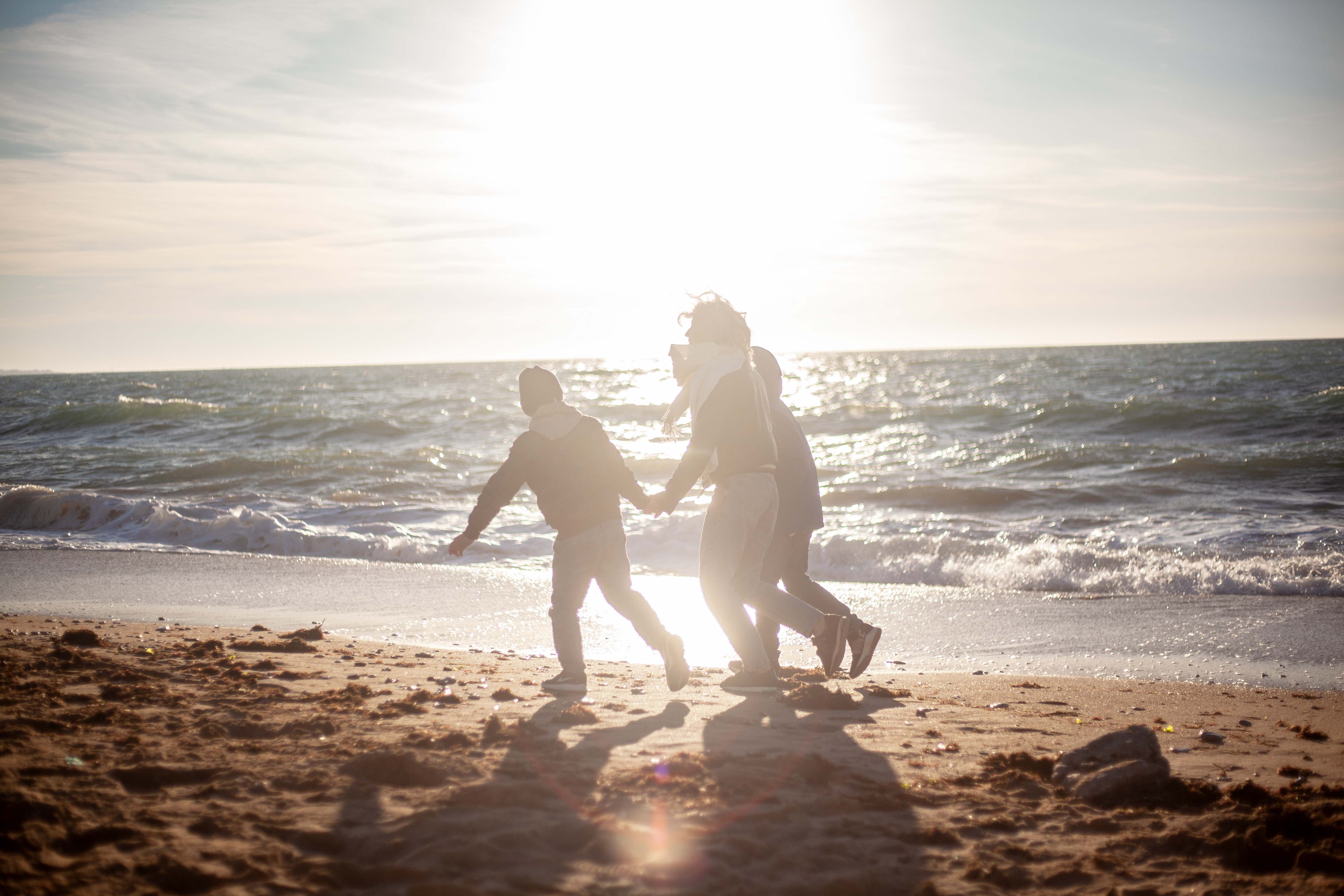 Family walking along shoreline as the sun sets in background.