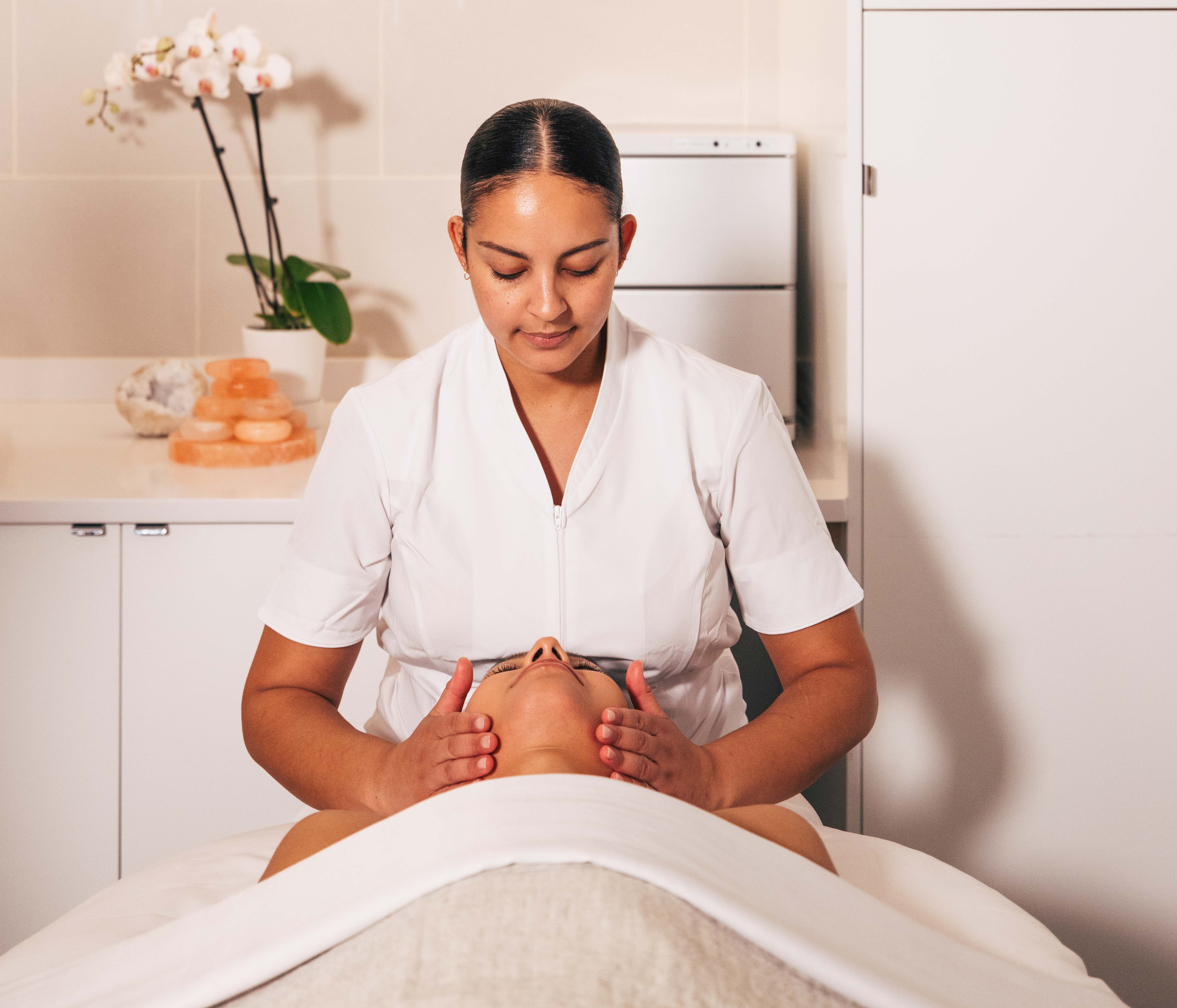 Woman giving a facial treatment to guest relaxing on table at Seawater Spa.