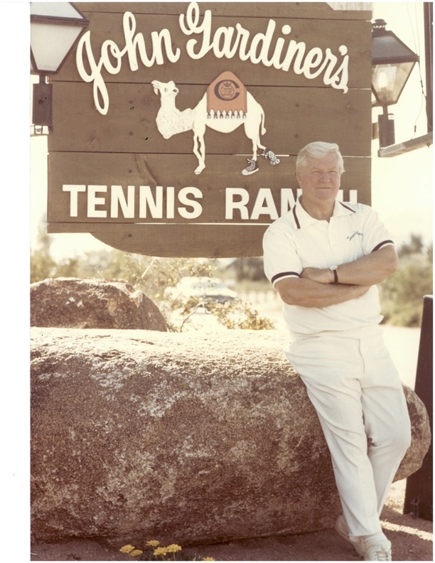 Photo of John Gardner standing in front of the John Gardner Tennis Ranch sign.