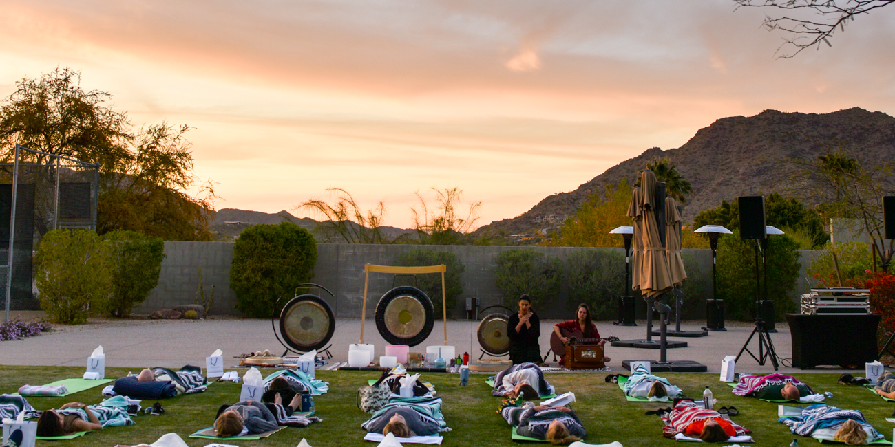 Sound meditation class relaxing under blankets on spa lawn as sun sets.