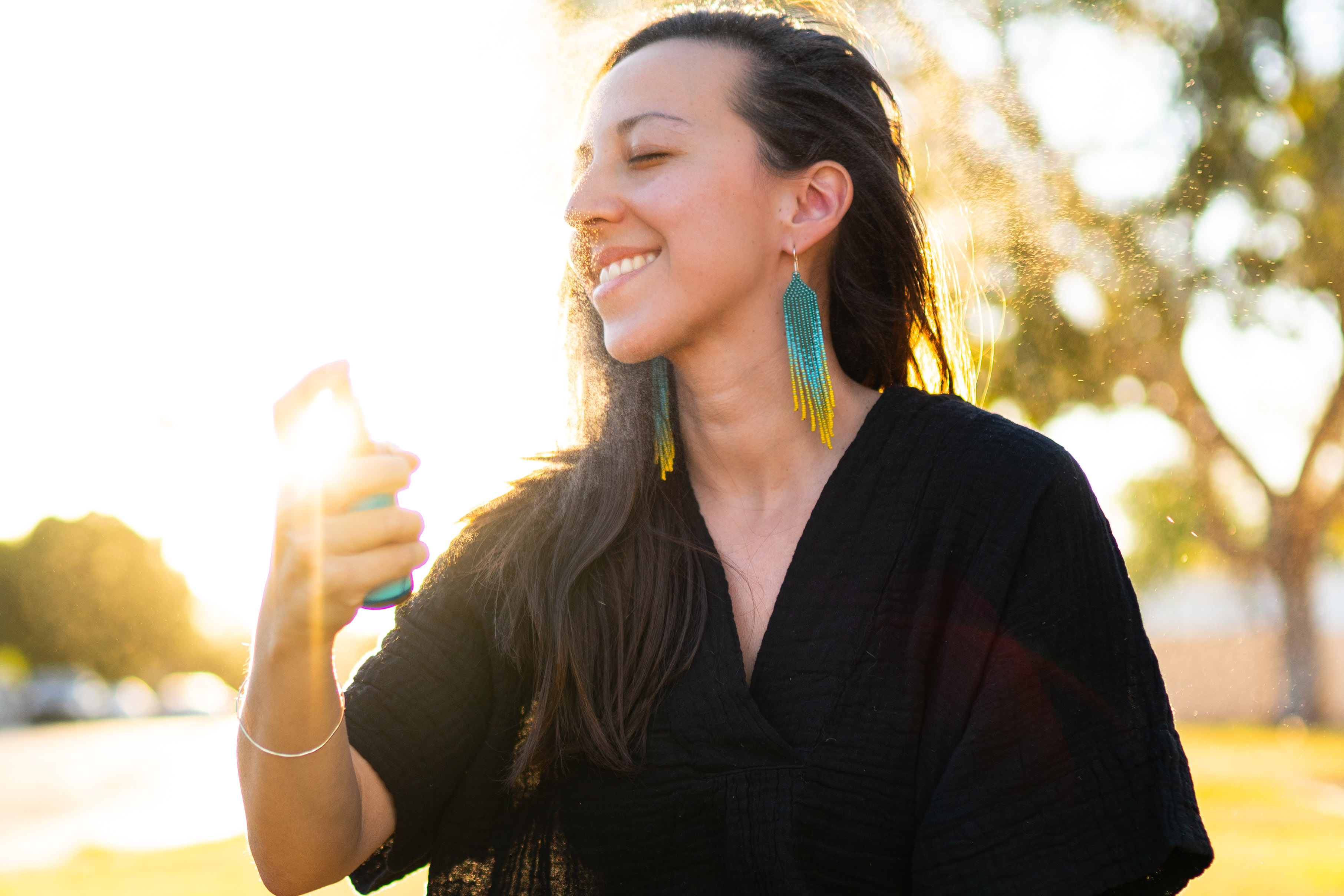 Woman sitting outside in sunshine happily misting her face with LOTUSWEI products