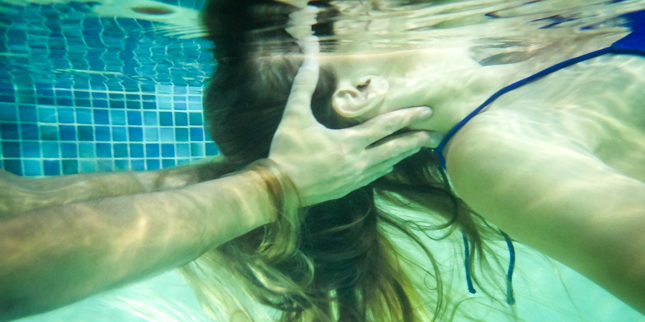 Woman floating in pool as Watsu therapist supports her head and neck underwater.