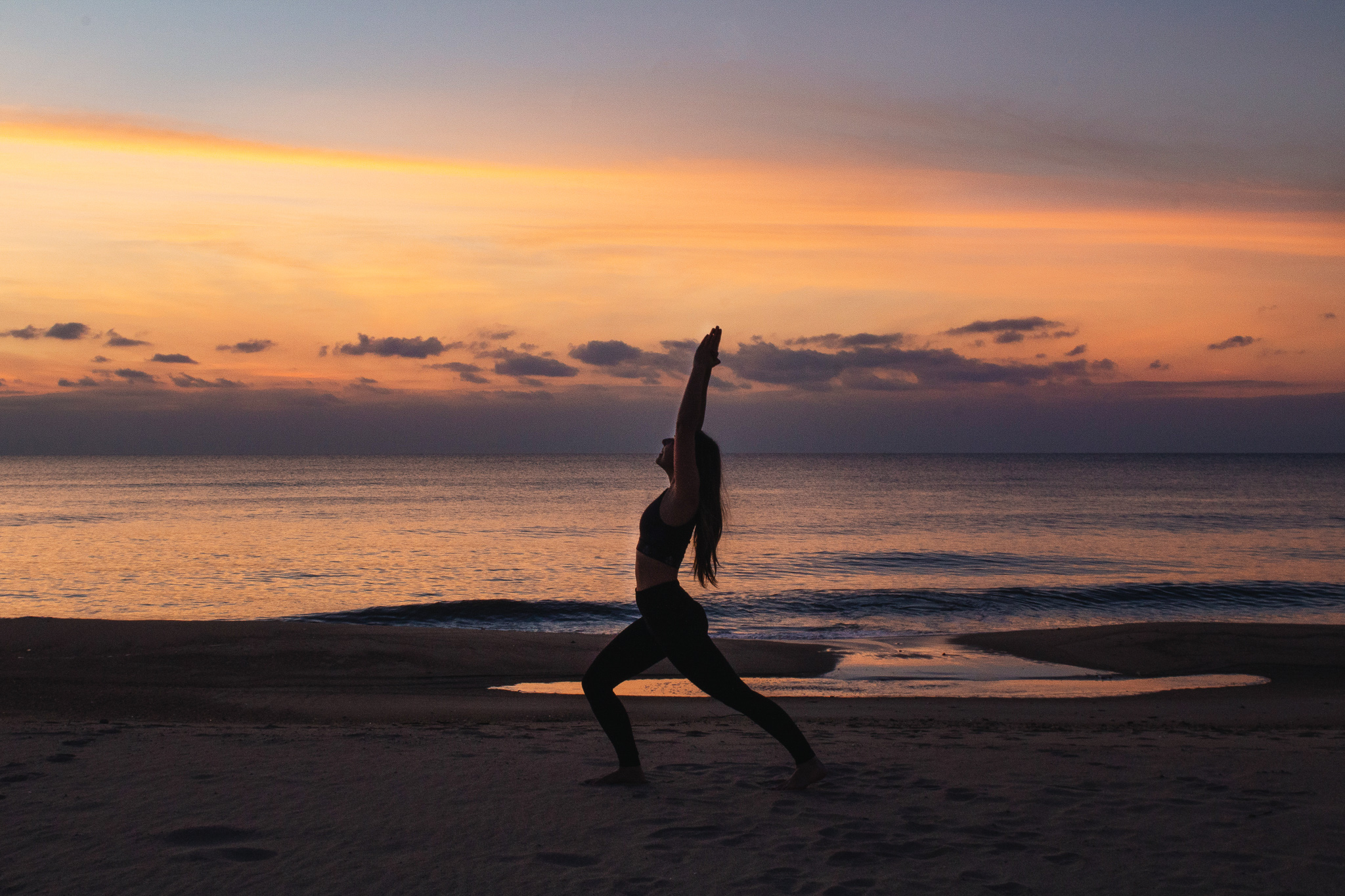 Woman doing yoga on the beach with stunning, colorful sunset in background.