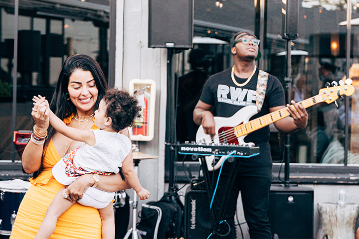 A woman dancing with a baby in front of a man playing electric guitar.