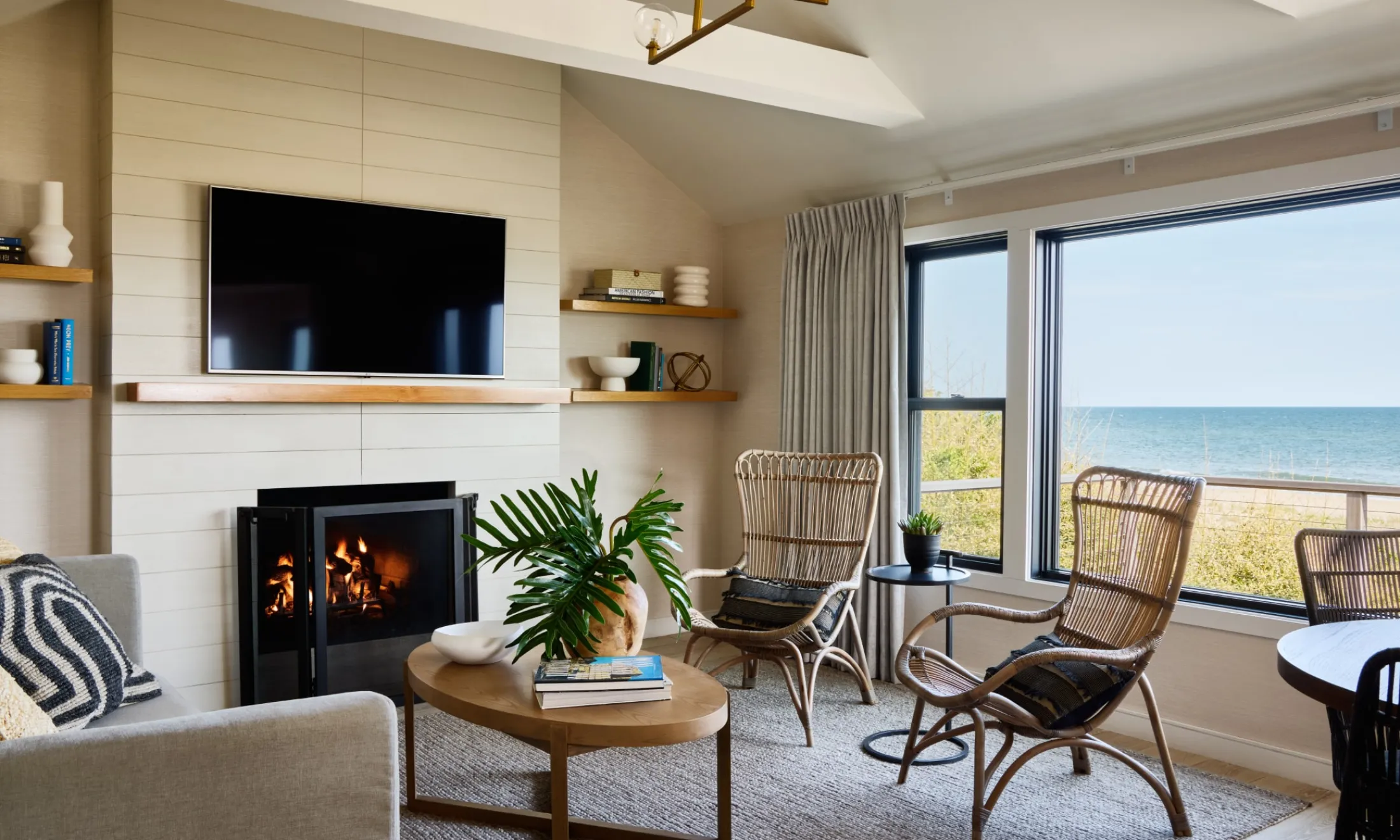 A cozy living room with a fireplace, TV, and seating area, featuring a large window with a ocean view.