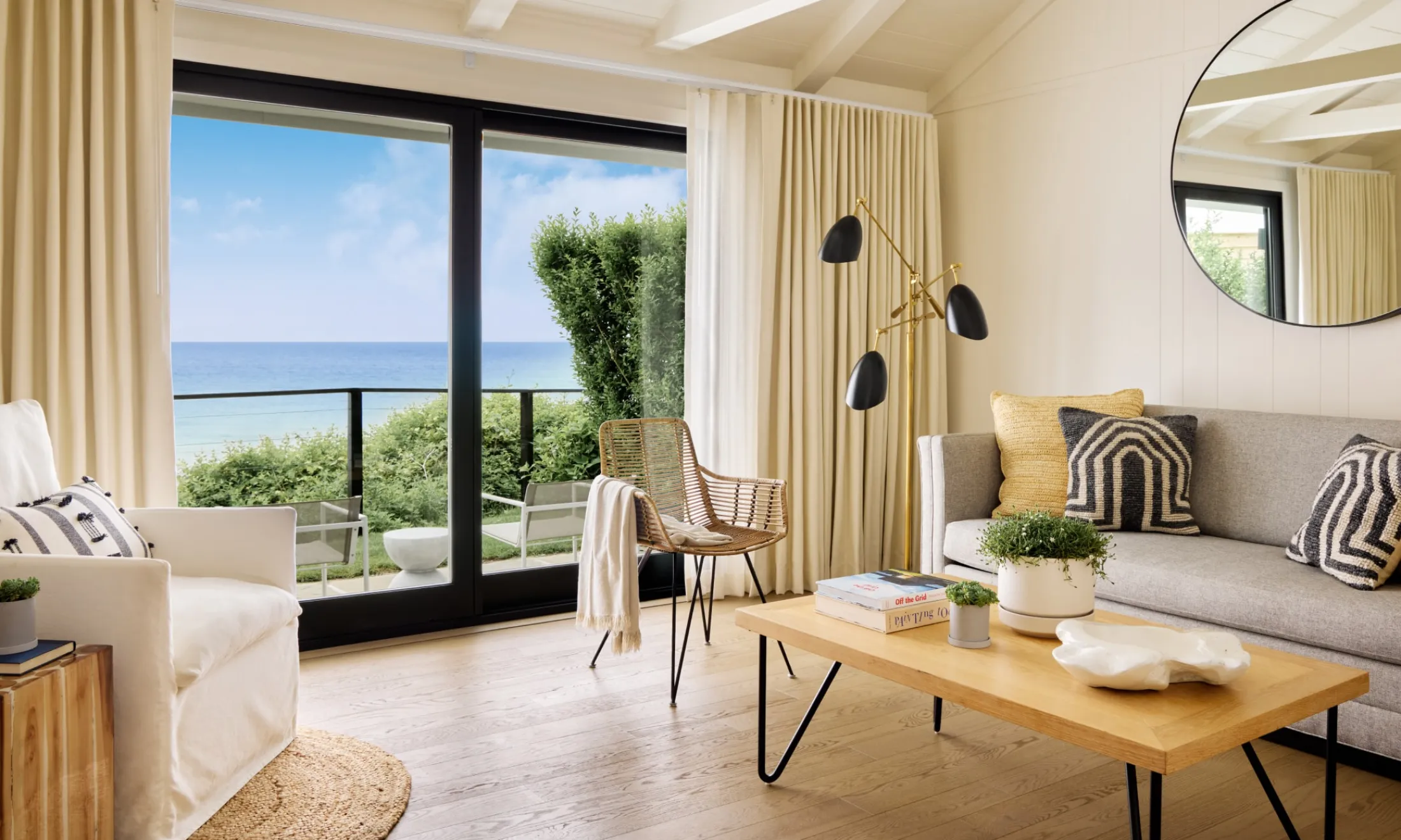 A living room with a gray sofa, a wooden coffee table, a white armchair, and a balcony with a view of the ocean.