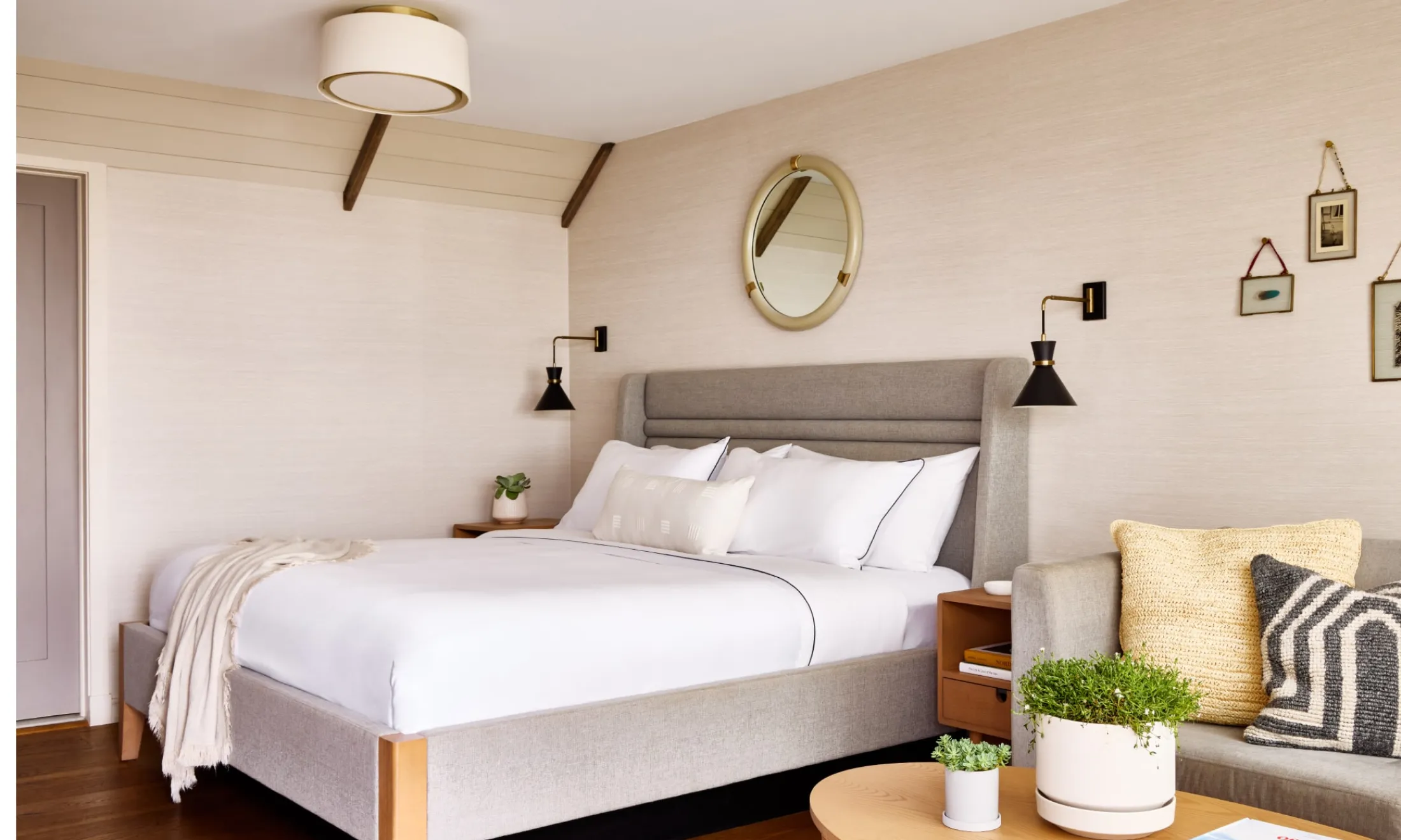 A wide view of a hotel room with a king-sized bed, a sofa, a coffee table with plants, and a mirror on the wall.