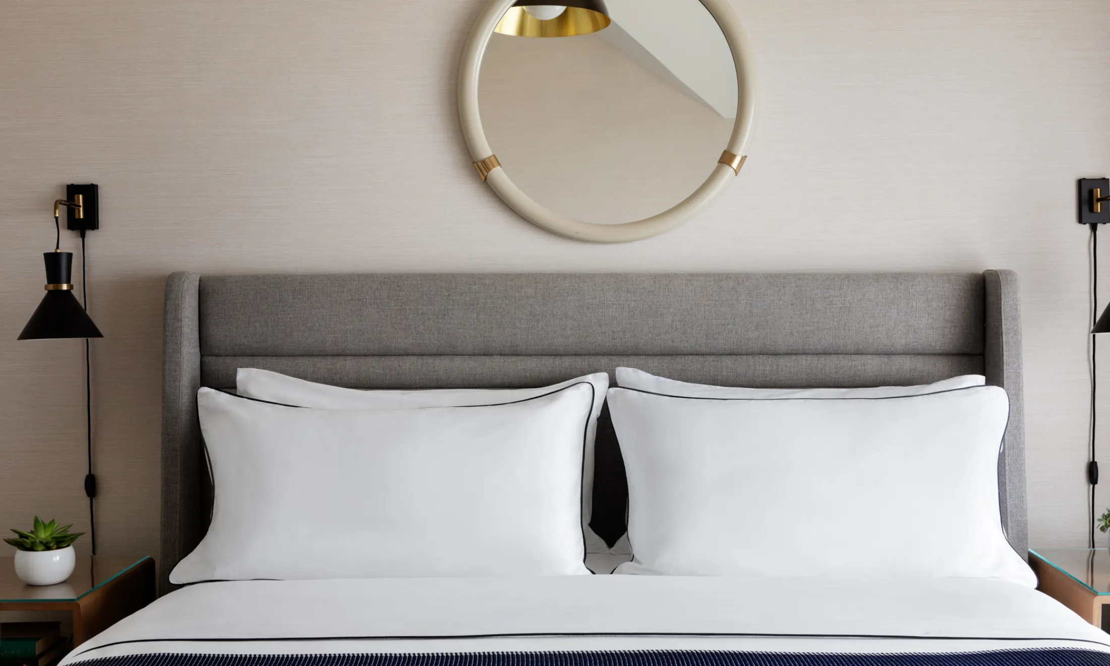 a neatly made bed with white linens and a gray headboard