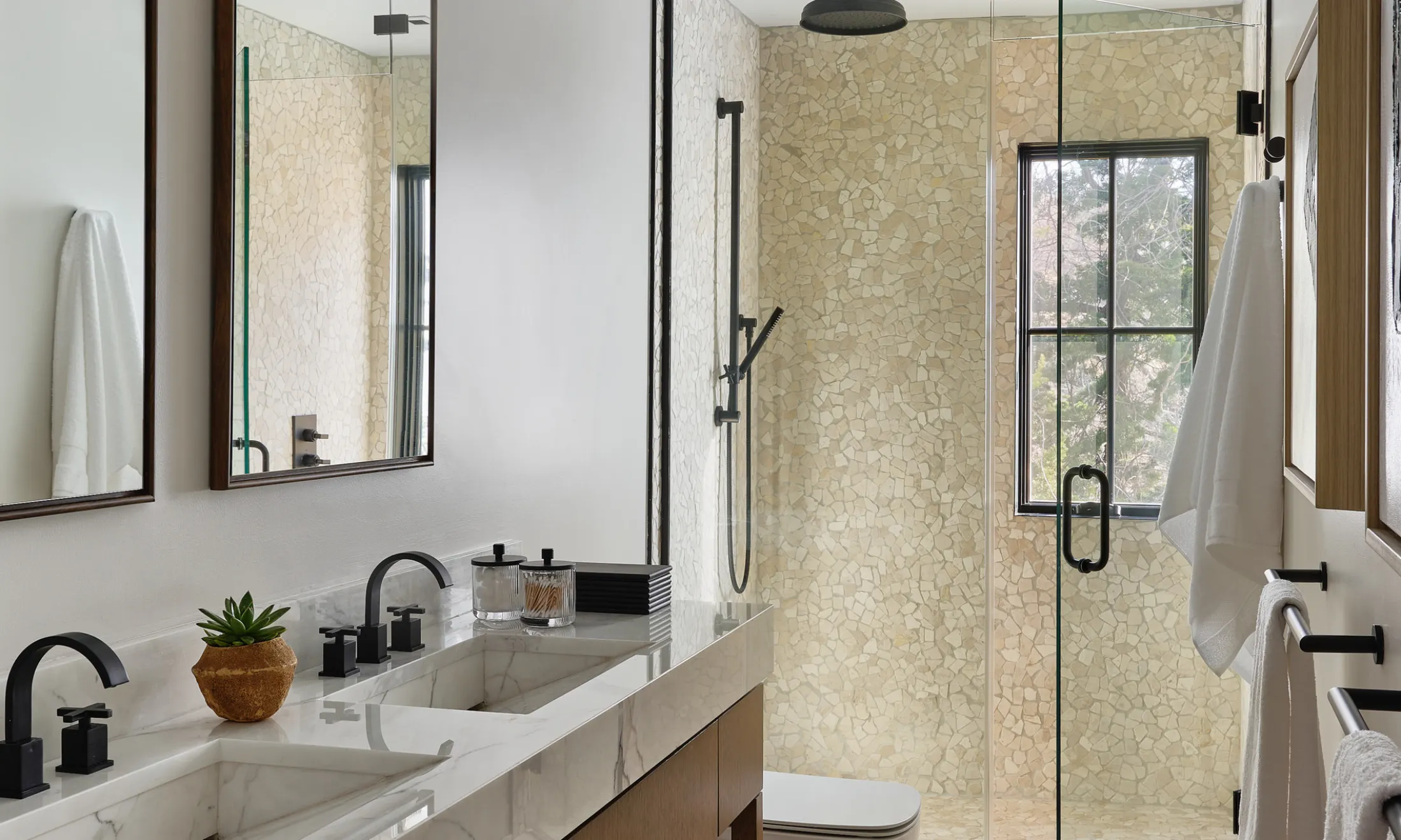 A modern bathroom with a large mirror, double vanity, and glass-enclosed shower.