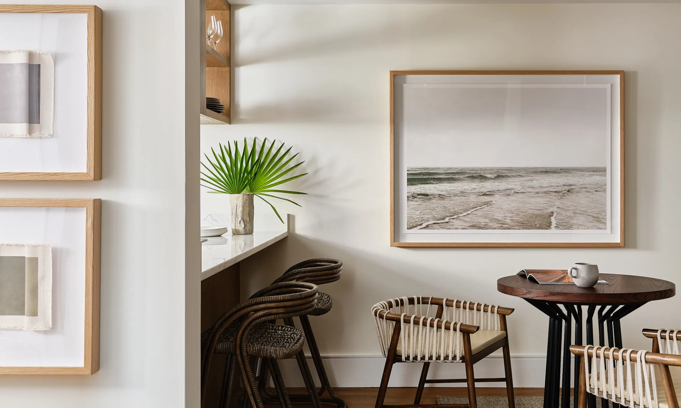 A small dining area with a round table and chairs, a counter with stools, and framed artwork on the walls.