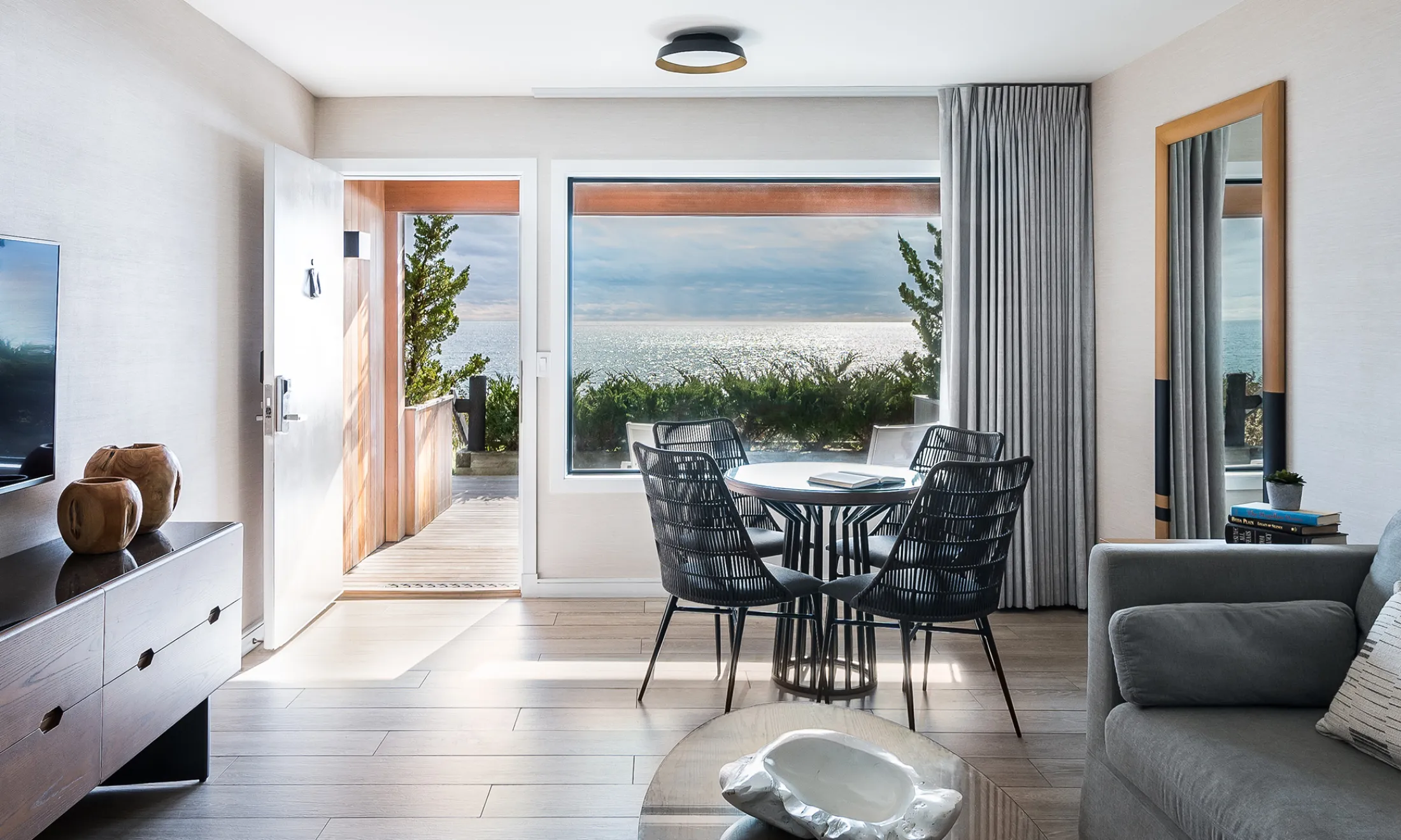 A wide view of a modern living room with a dining area, sofa, and balcony with an ocean view.