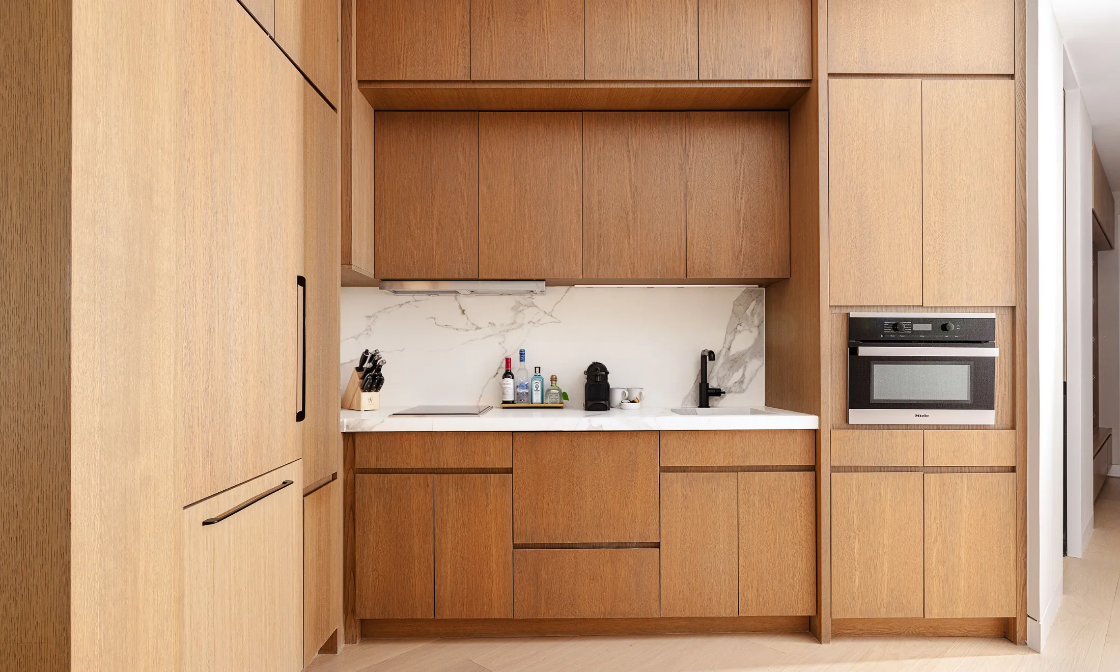 A modern kitchenette with wooden cabinets, marble backsplash, and stainless steel appliances.