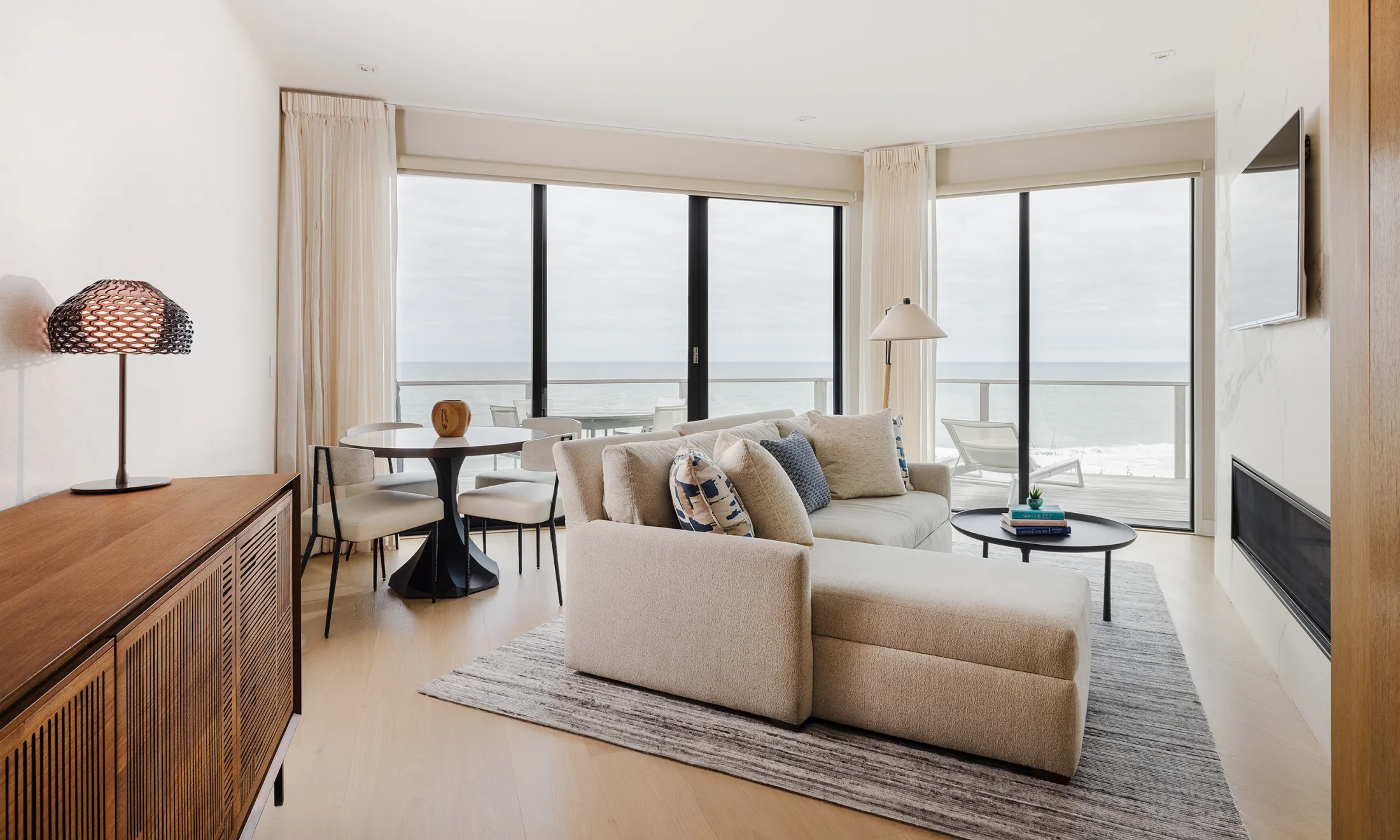 A wide view of a modern living room with a sofa, coffee table, dining table, and balcony.