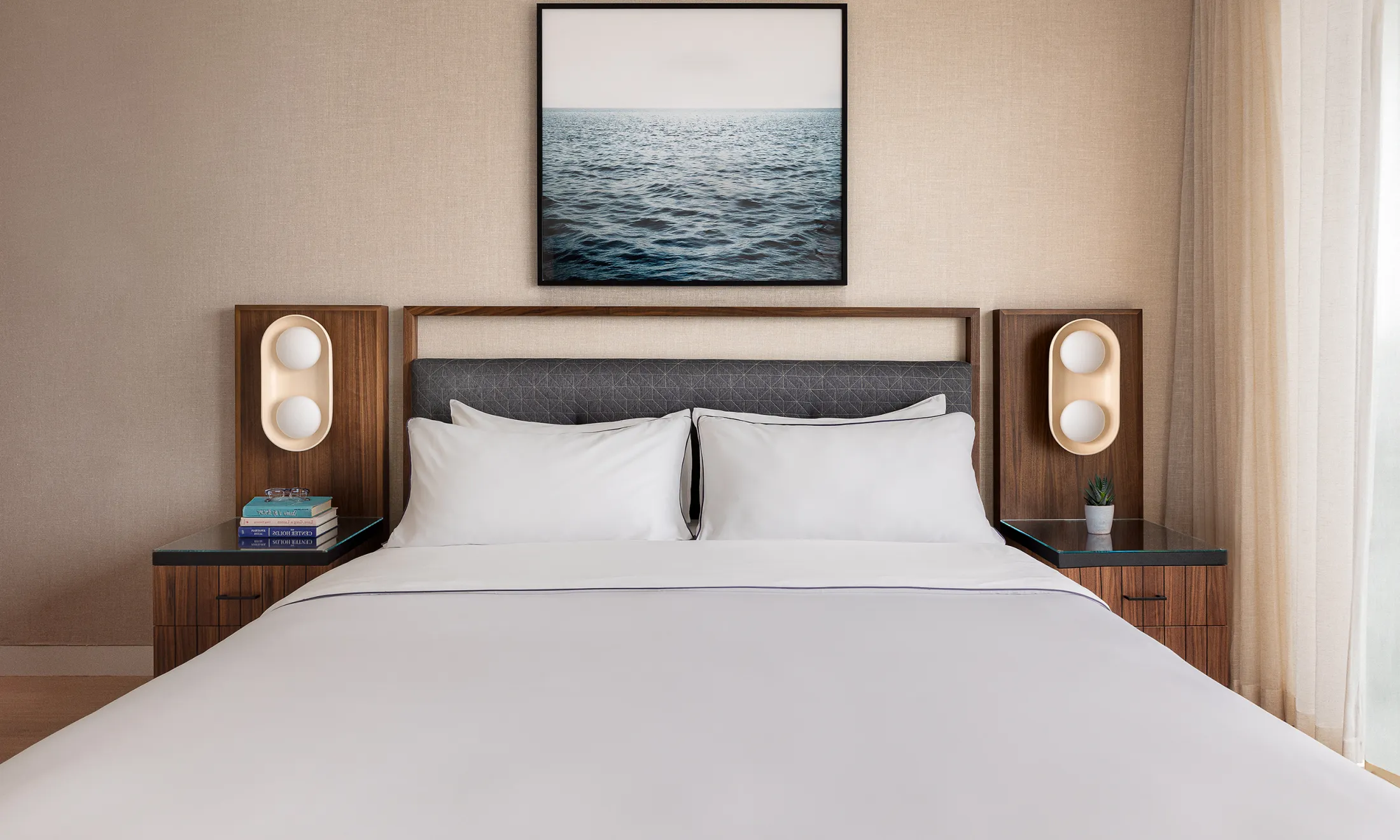 A neatly made bed with white linens and pillows in a room with a large headboard and nightstands.