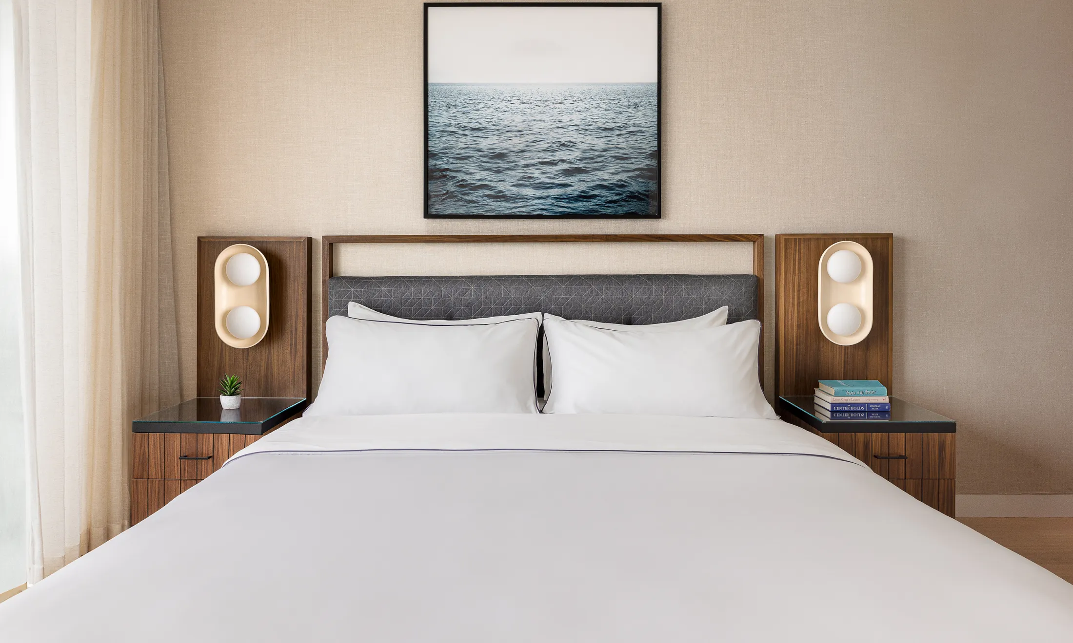 A neatly made bed with white linens and pillows in a room with a large headboard, nightstands, and a picture above the bed.