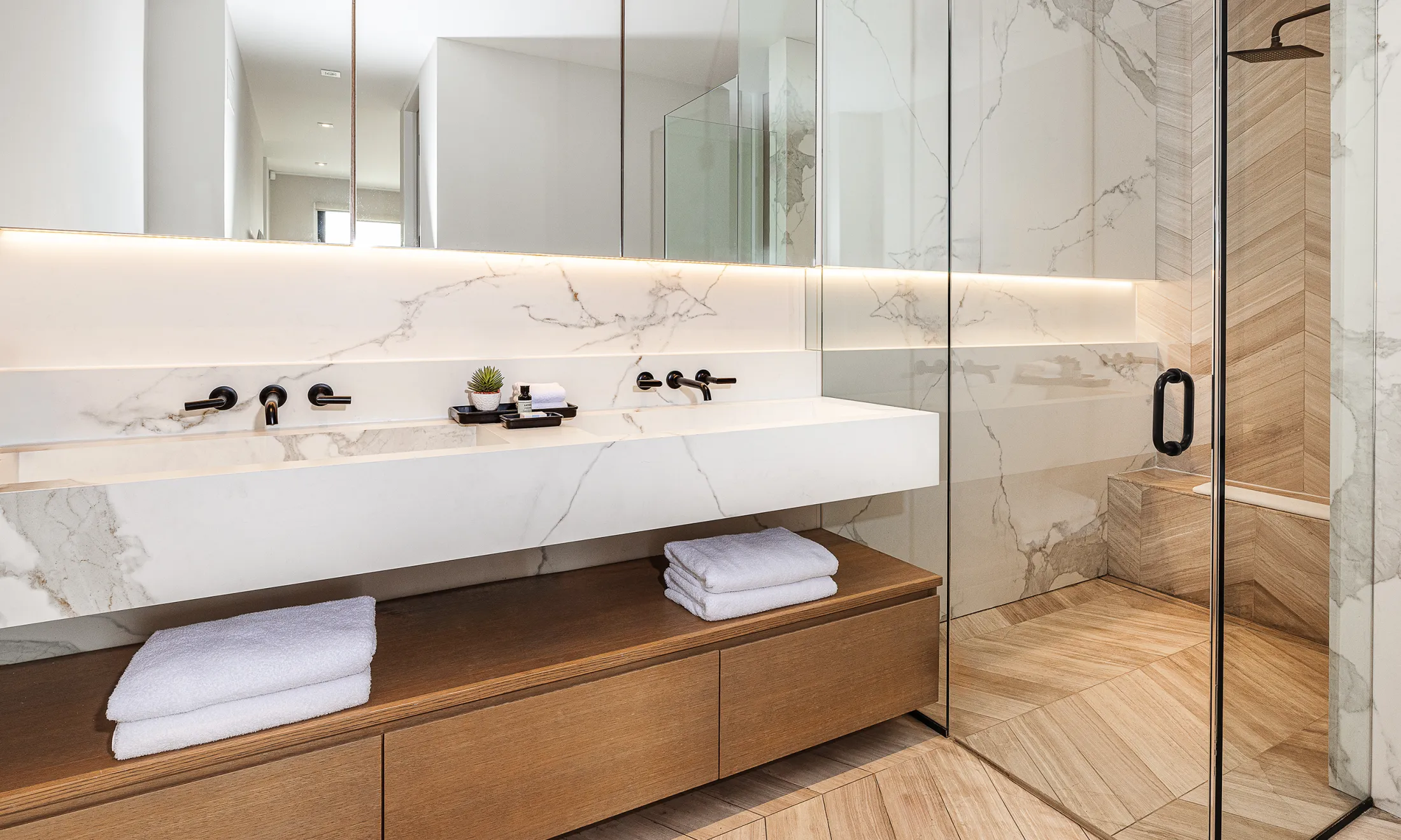 A modern bathroom with a marble sink, glass shower door, and wooden accents.