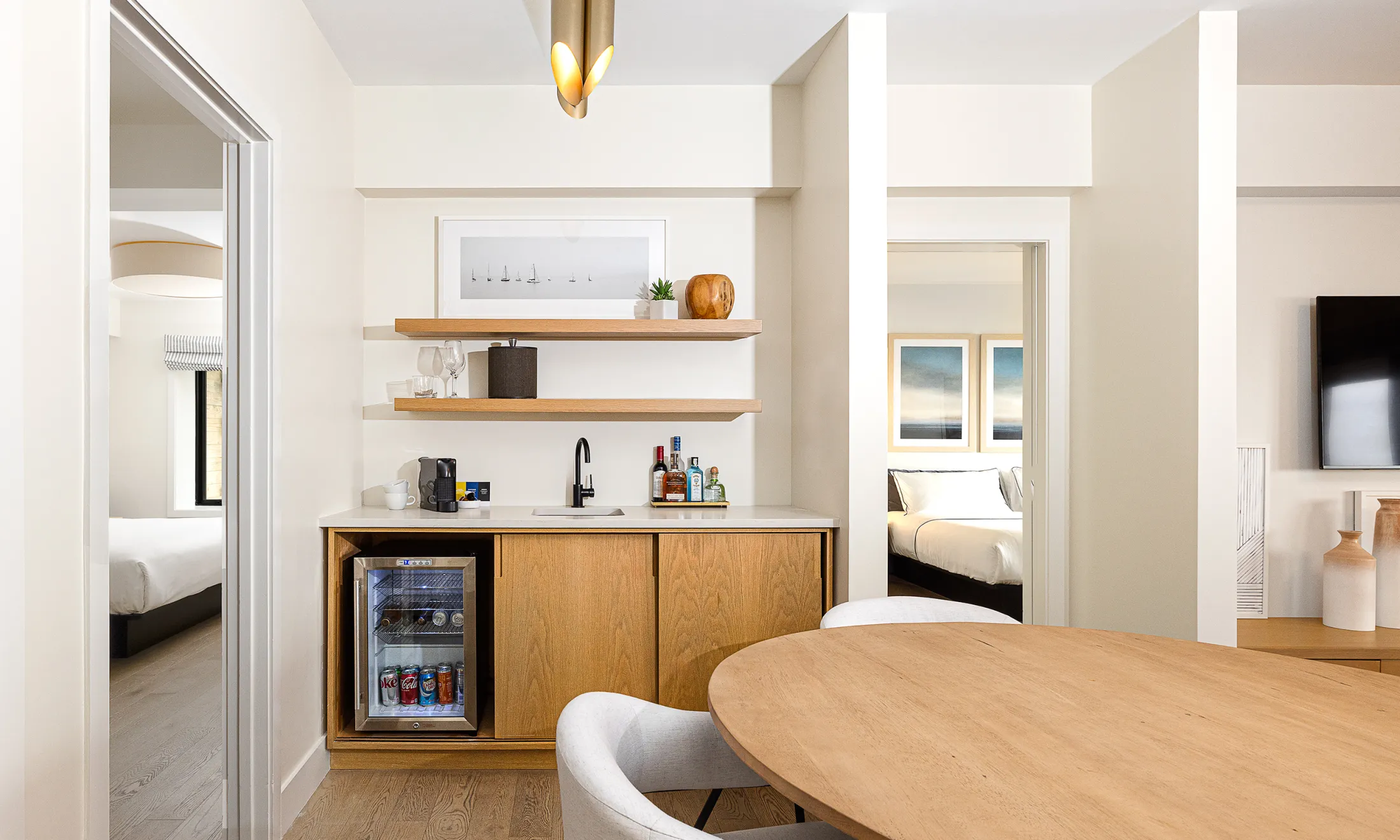 A modern hotel suite with a kitchenette, dining table, and mini fridge.