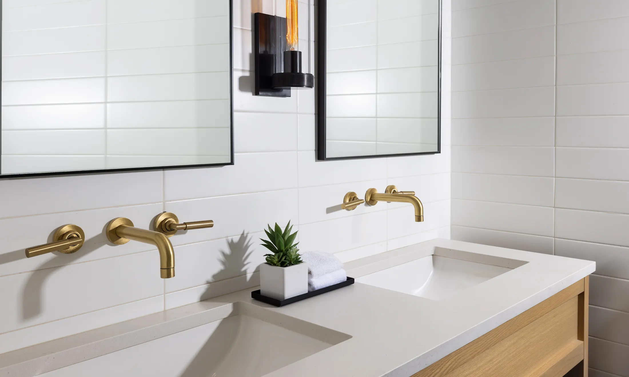 A modern bathroom with a double vanity, two gold faucets, and two mirrors.