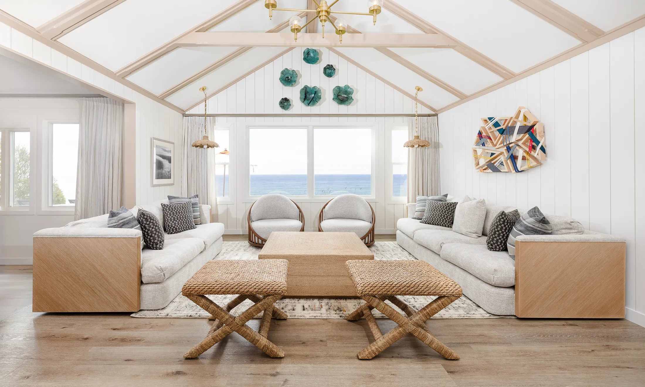 A wide view of a bright, beach-style living room with vaulted ceilings and large windows showing the ocean.