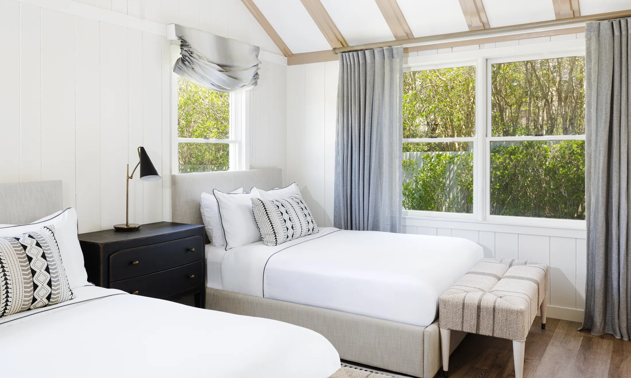 A bright and airy room with two beds, a window, and a bench.
