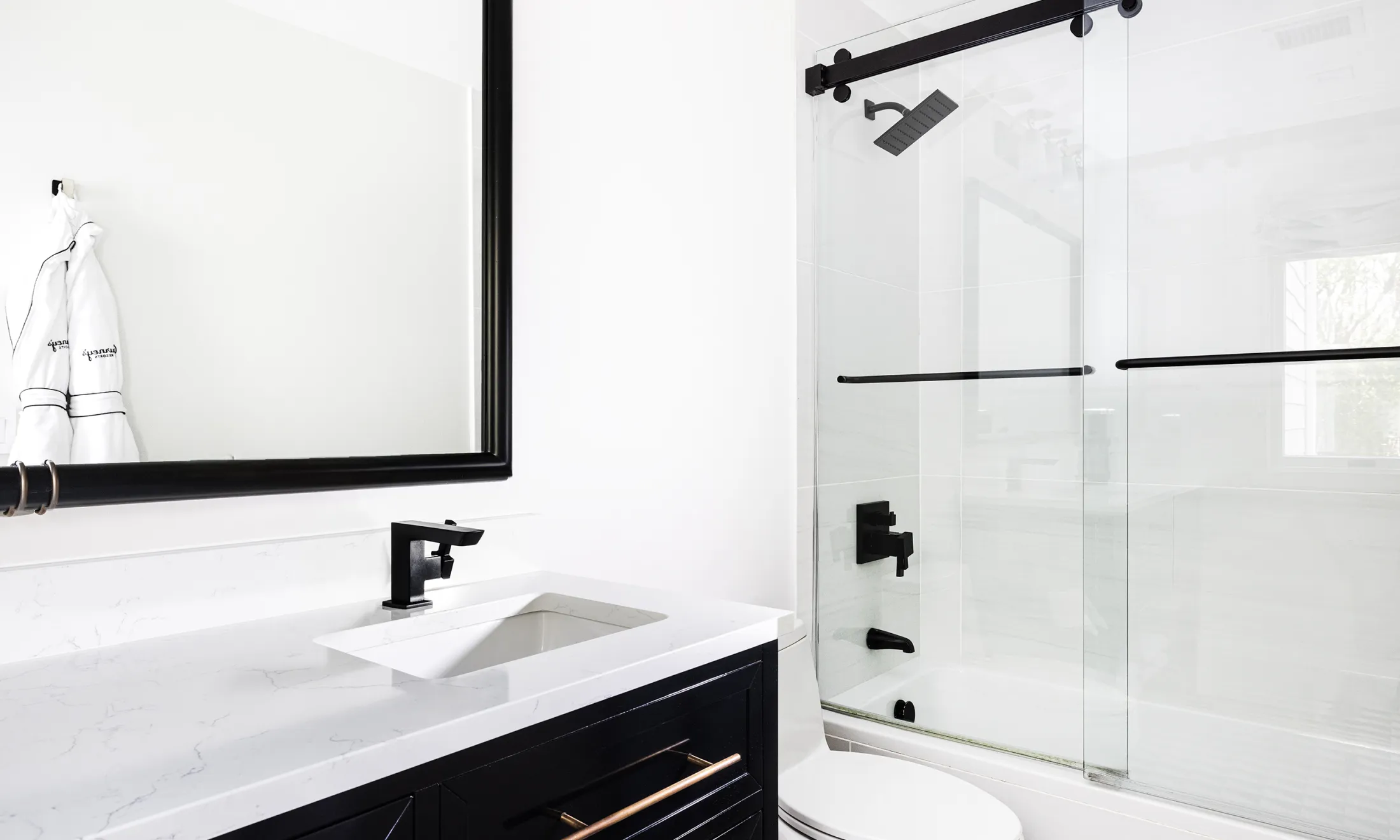 A modern bathroom with a white marble countertop, black fixtures, and a glass shower door.