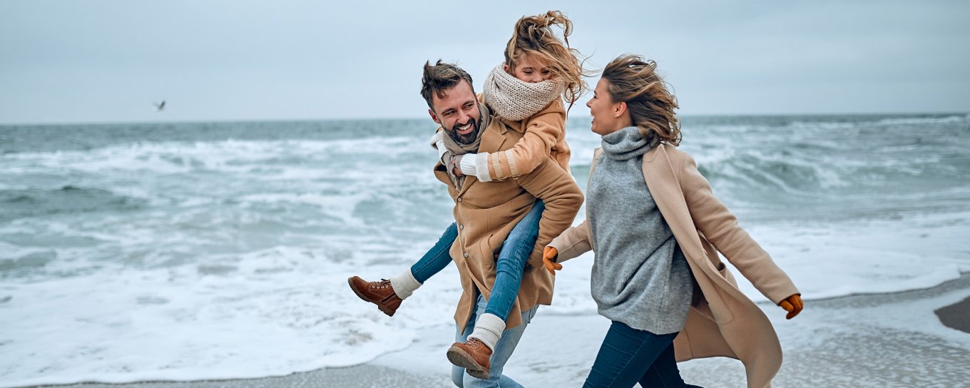 Family of three walking on the beach in winter clothing