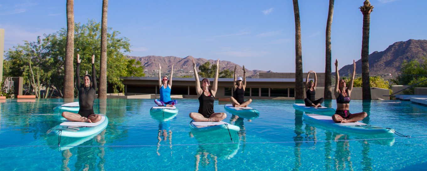 A group of people balancing on paddleboards in a pool.