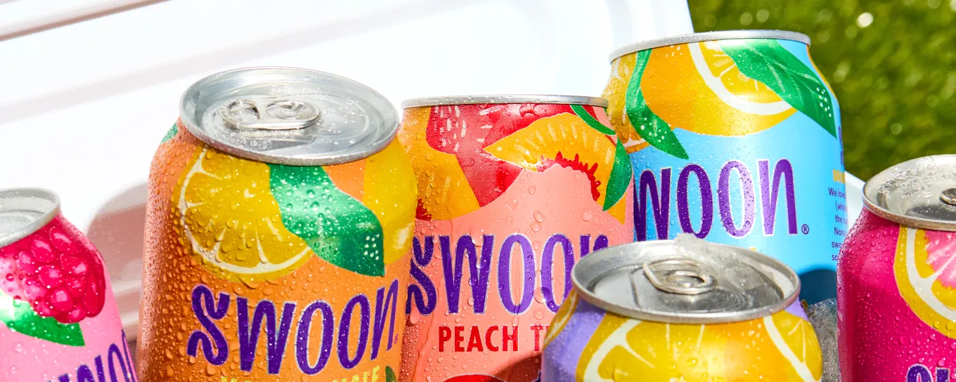 A cooler filled with brightly colored Swoon lemonade cans with grass in the background