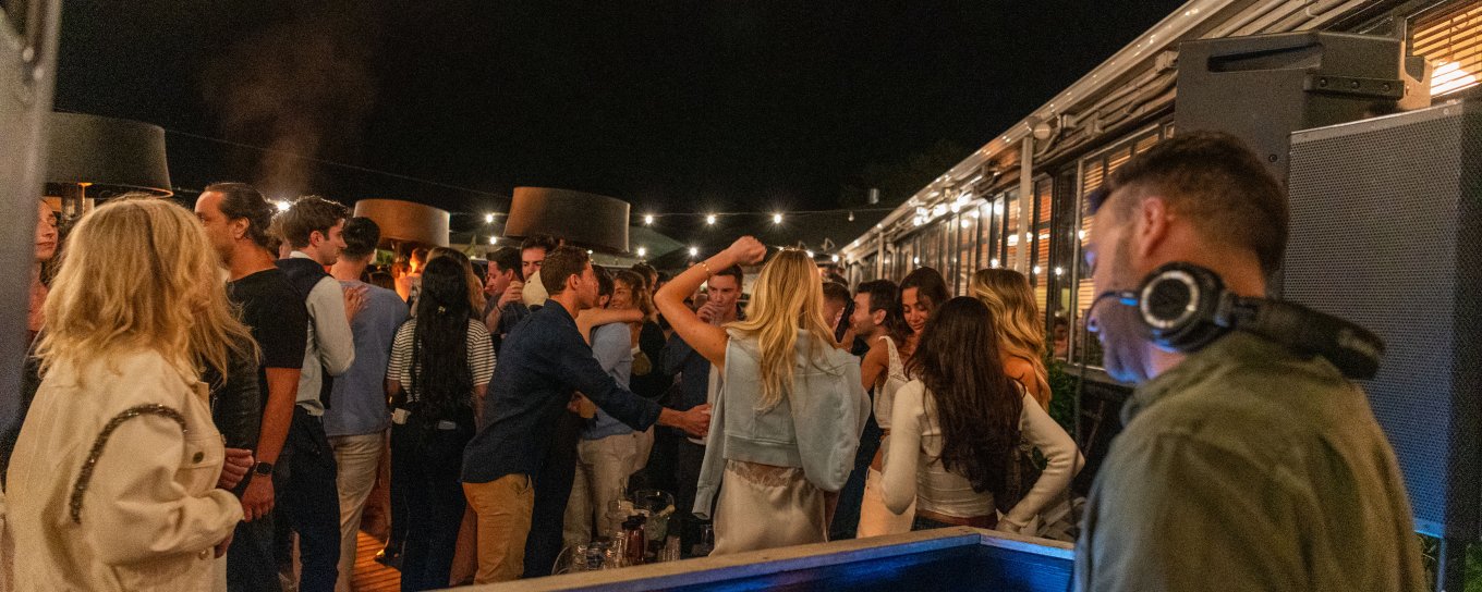 DJ playing music at an outdoor night party, with a crowd dancing under string lights.