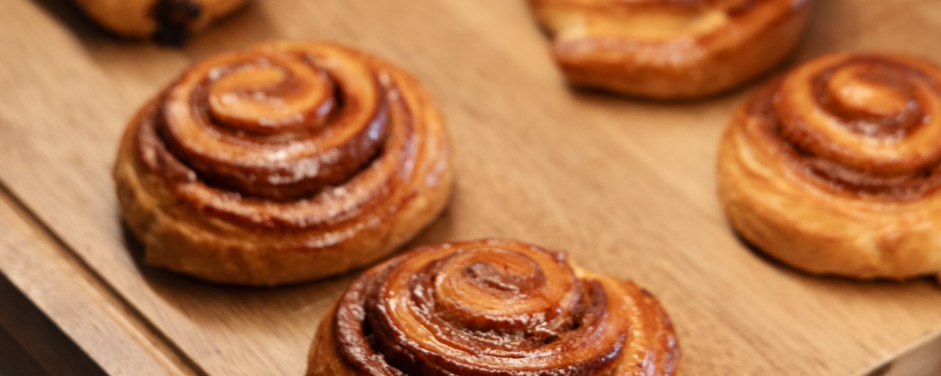 Freshly baked pastries, including golden-brown cinnamon rolls and croissants, arranged on a wooden tray.