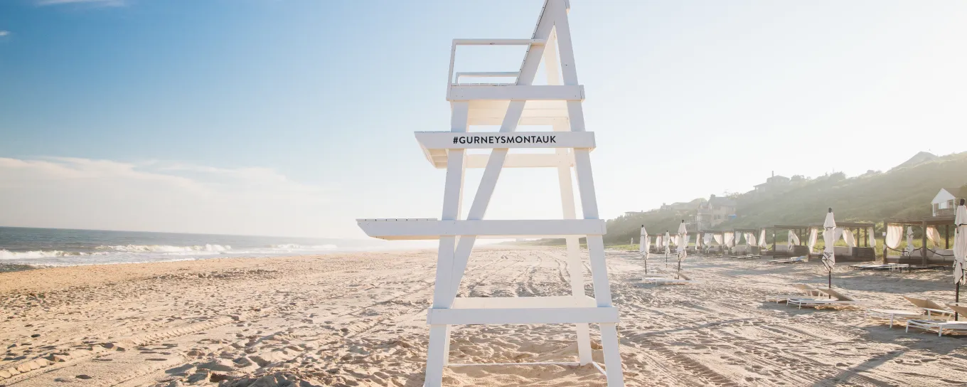 Lifeguard chair on a sunny beach, with a clear blue sky and the ocean to the left.