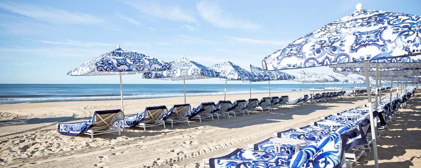 Beach scene with rows of blue-patterned umbrellas and loungers on sandy shore under a clear sky.