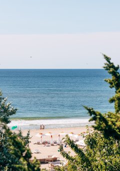 Two evergreen trees in the foreground frame the beach at Gurney's Montauk Resort