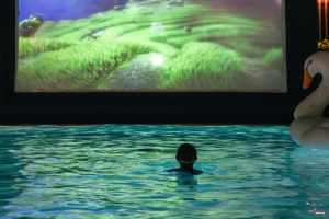 A child bobs in a pool in front of a bright screen