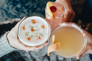 Three hands holding brightly colored cocktails in a cheers