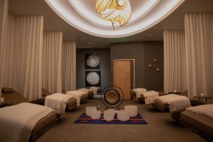 Spa relaxation room with several lounge chairs draped in white towels, warm lighting, and decorative artwork on the walls.