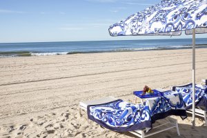 Beach with patterned blue loungers and umbrella on white sand, facing the calm sea under a clear sky.