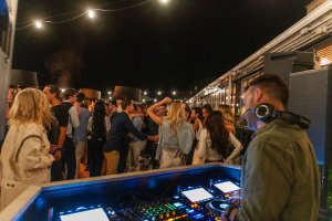 DJ playing music at an outdoor night party, with a crowd dancing under string lights.